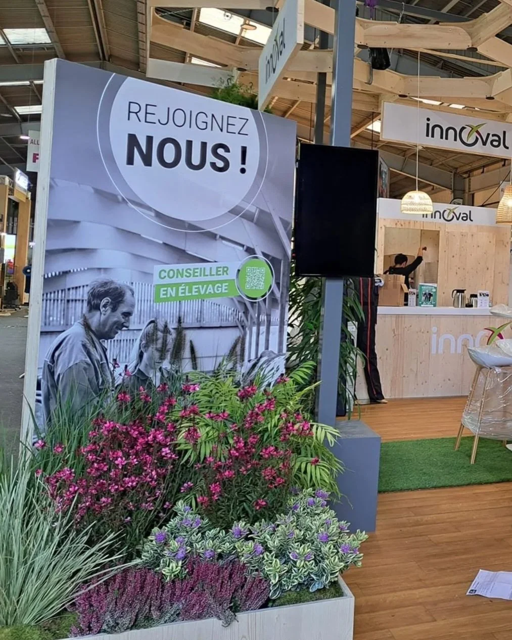 Panneau publicitaire avec texte en français «Rejoignez-nous!», et une image en noir et blanc d'une personne avec un animal, entourée de plantes fleuries dans un espace d'exposition intérieur.