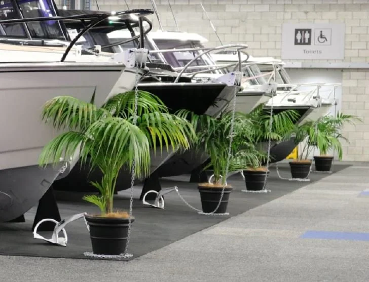 Quatre yachts dans un entrepôt, entourés de plantes en pot, avec un signe indiquant des toilettes à l'arrière.