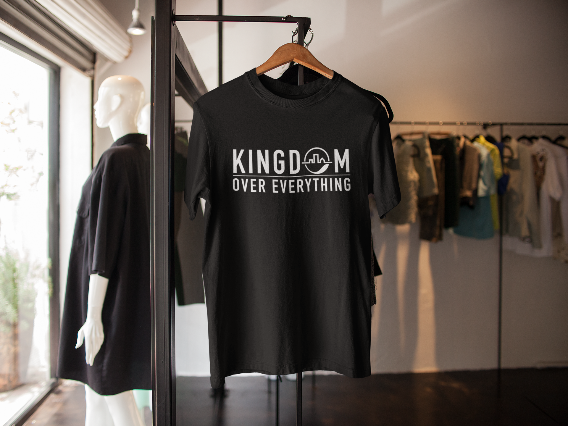Black T-shirt hanging on a wooden hanger, displayed on a clothing rack in a store with other garments visible in the background.