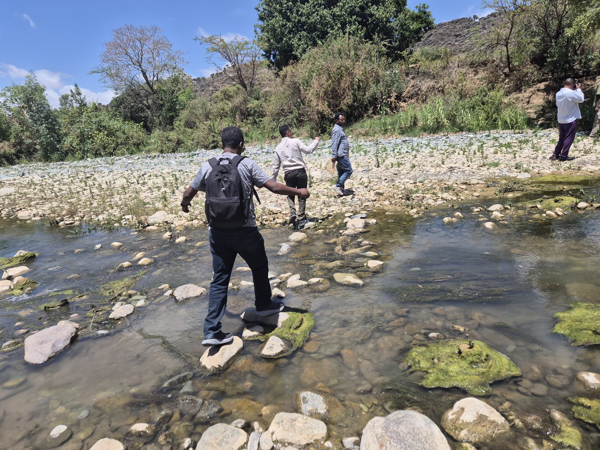 Community members crossing a restored river in Wukro, Tigray, where indigenous planting and erosion control support healthier riverbanks.