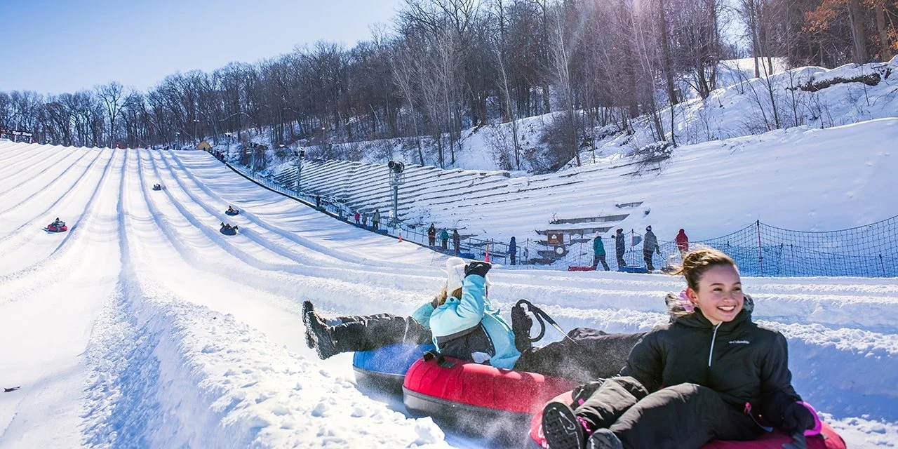 Children enjoying snow tubing down a snowy hill at a winter resort.