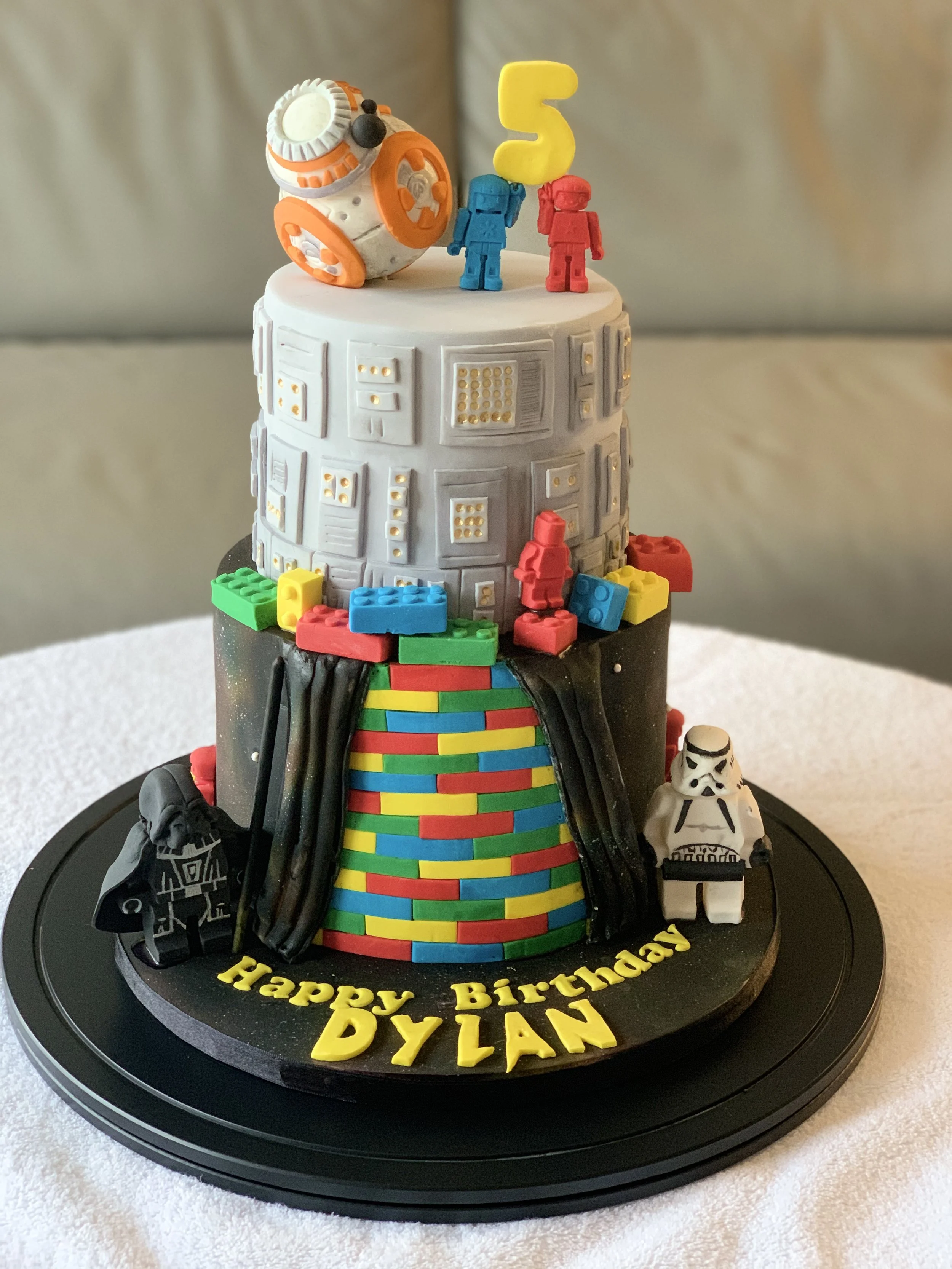 Star Wars themed birthday cake with figurines, LEGO bricks, and a BB-8 cake topper, decorated with the message 'Happy Birthday Dylan'.