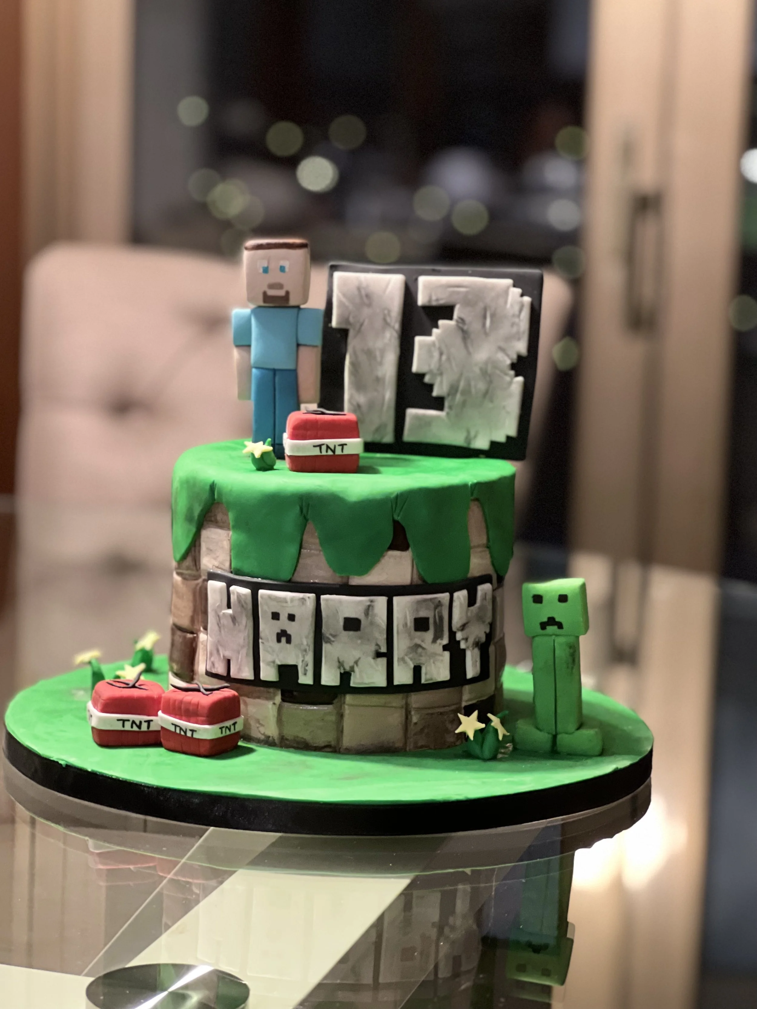 A Minecraft-themed birthday cake with a pixelated character, TNT blocks, and the number 13 on top, decorated with green grass-like fondant.