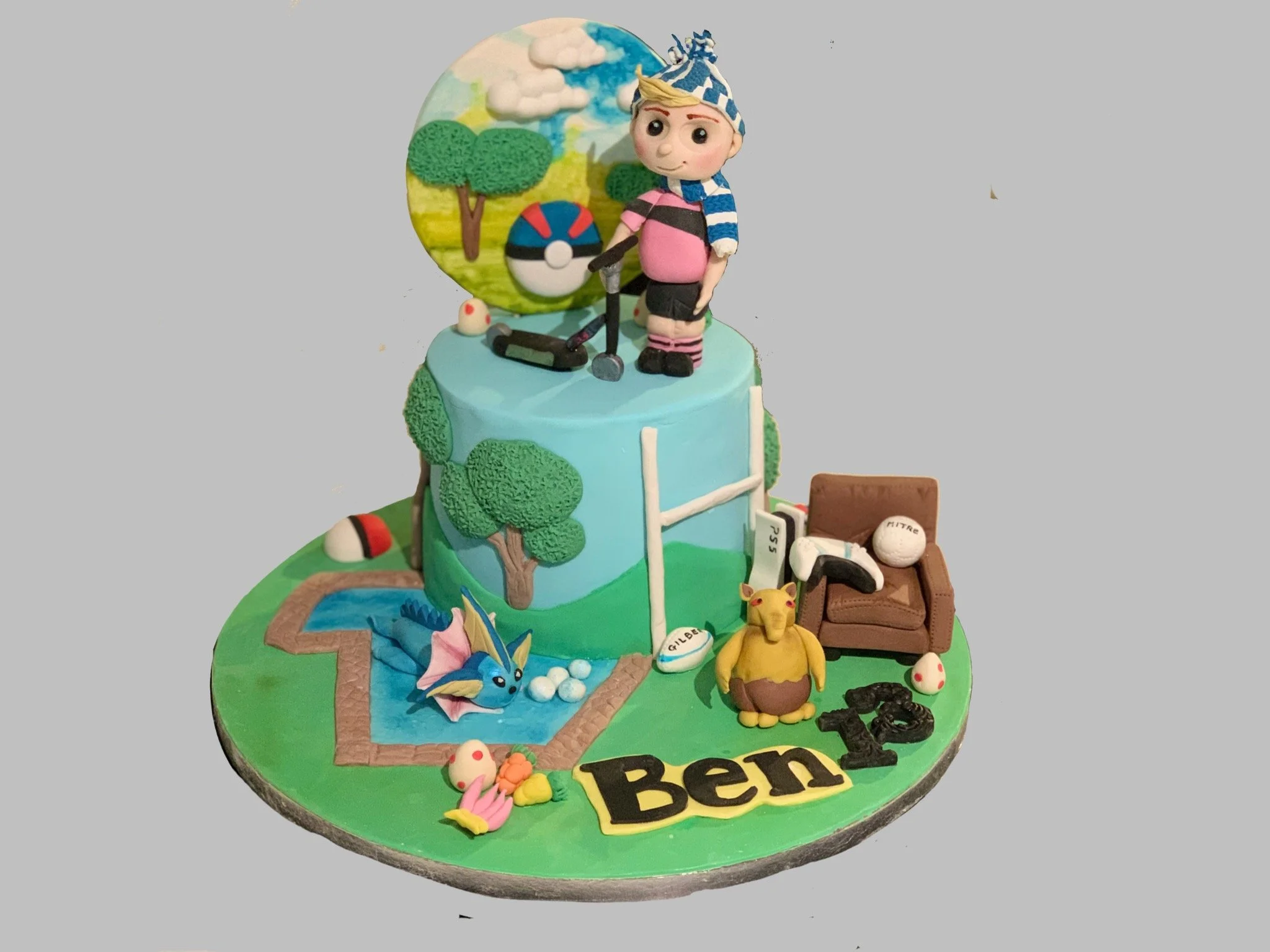 A themed cake celebrating a boy named Ben with Pokémon and sports decorations. The cake features a figurine of a boy with a blue and white checkered hat, standing on top of a Pokémon-themed background. The lower part of the cake displays Pokémon figu