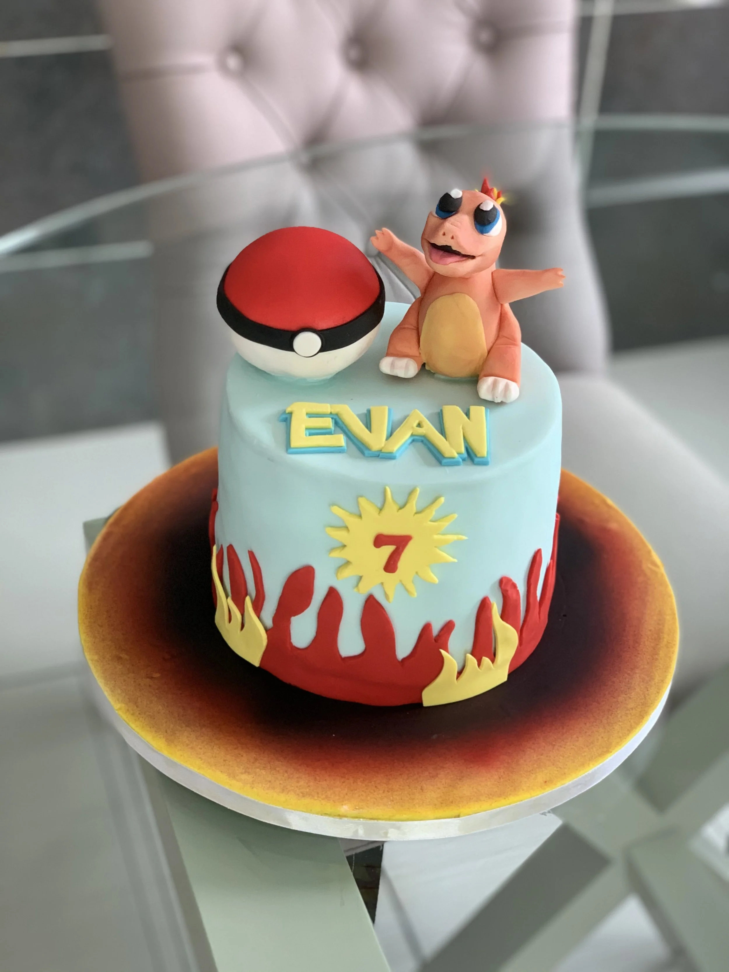 A Pokemon-themed birthday cake with a Charmander topper, a Pokeball, the name Evan, and the number 7. The cake has red and yellow flame decorations at the base.