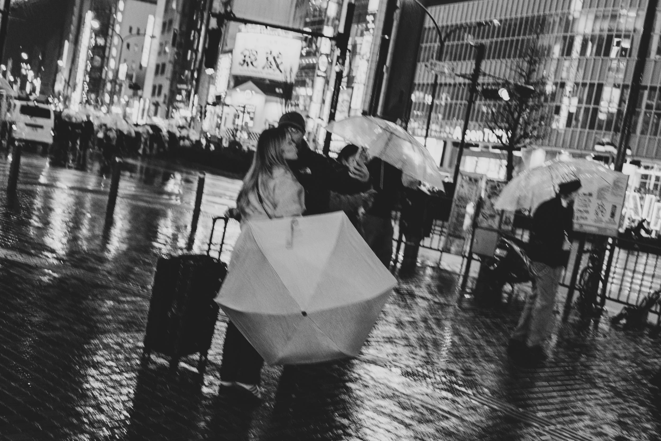 雨の日の都会の街角で人々が傘をさして歩いている様子。