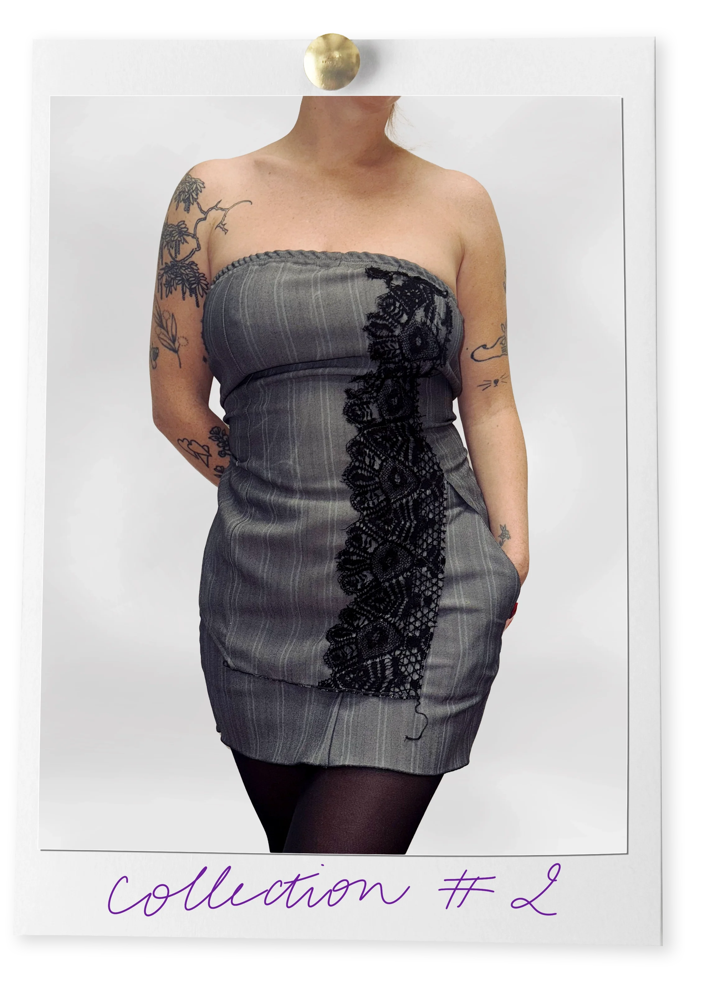 Une femme portant une robe grise à rayures avec des dentelles noires, des tatouages sur les bras, et habillée de collants noirs, en pose devant un fond blanc.