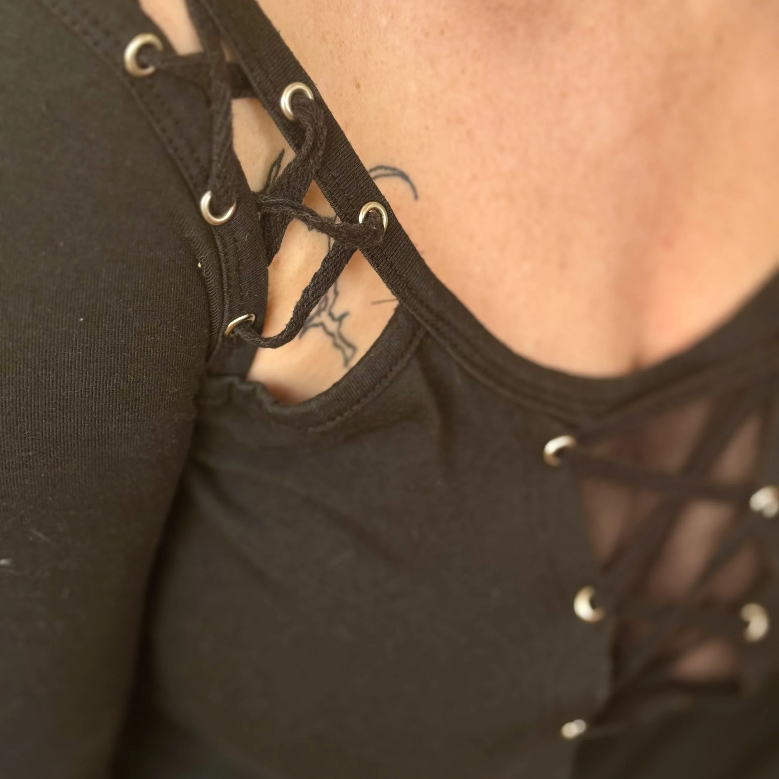 Zoom sur le décolleté d'une personne portant un haut noir à lacets avec des anneaux métalliques.