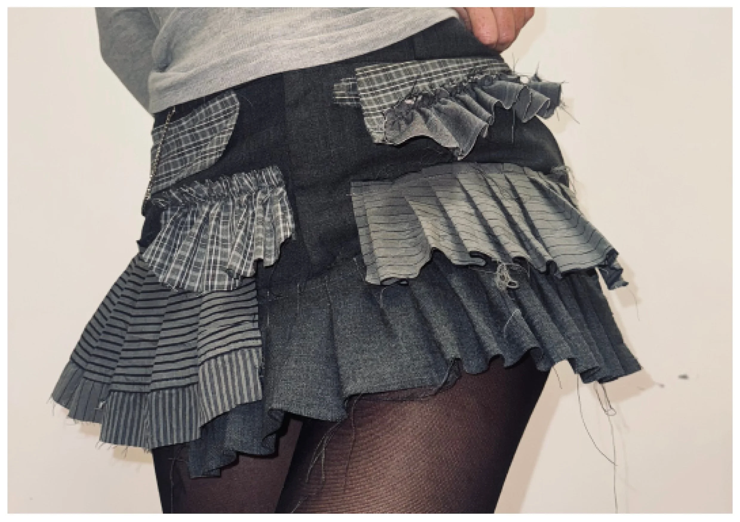 Jupon en jean à plusieurs couches avec des plis en tissu à carreaux et rayés, porté avec des collants en résille.