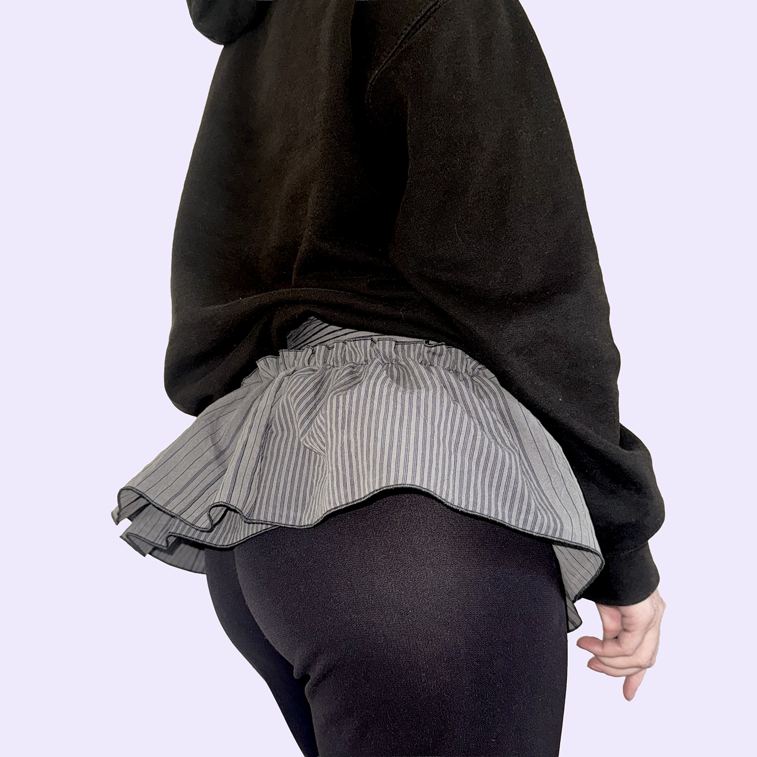 Femme portant une jupe plissée rayée et un pull noir, vue de derrière.