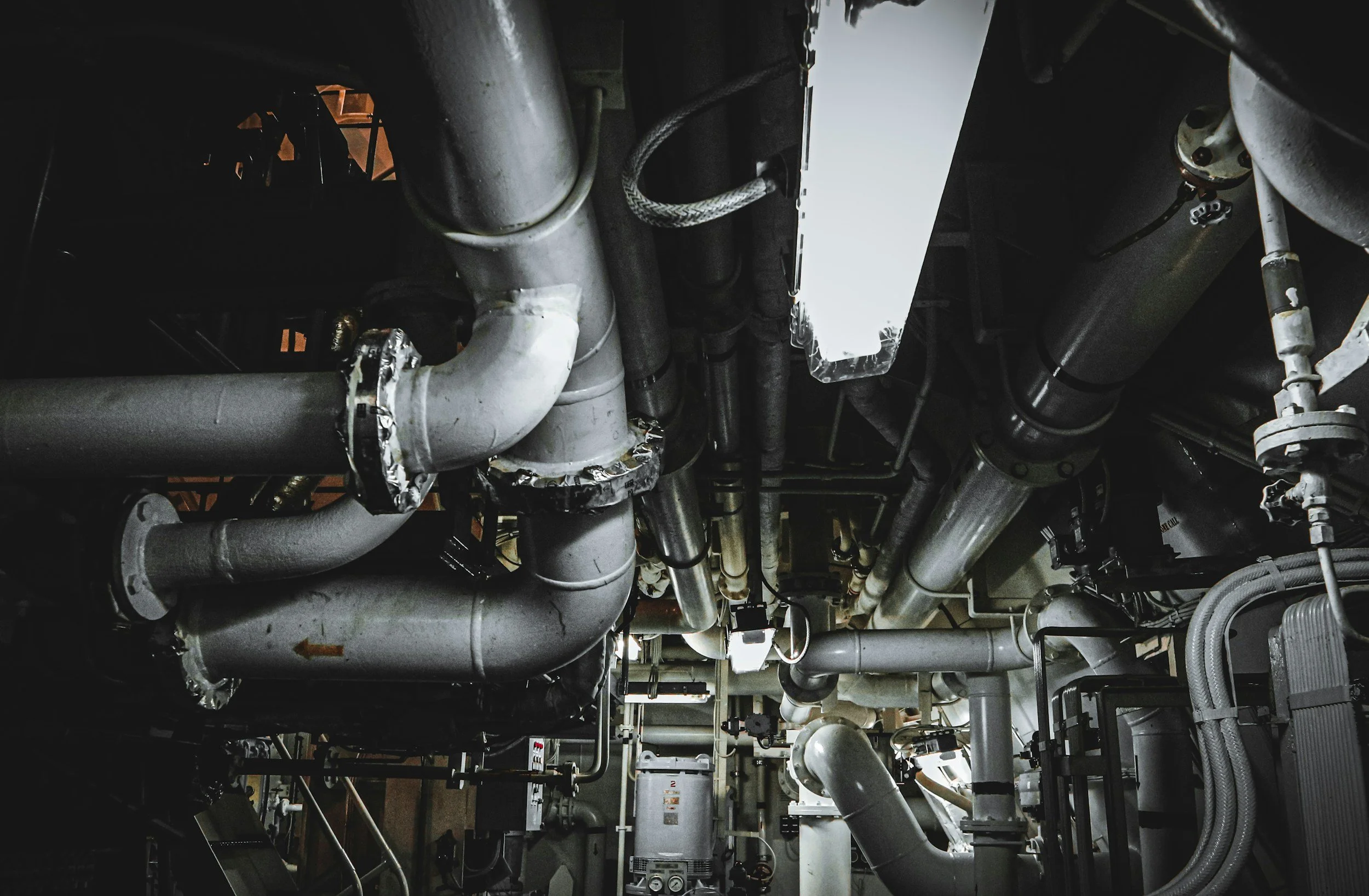 A complex network of silver and gray industrial pipes and machinery inside a mechanical or utility room.
