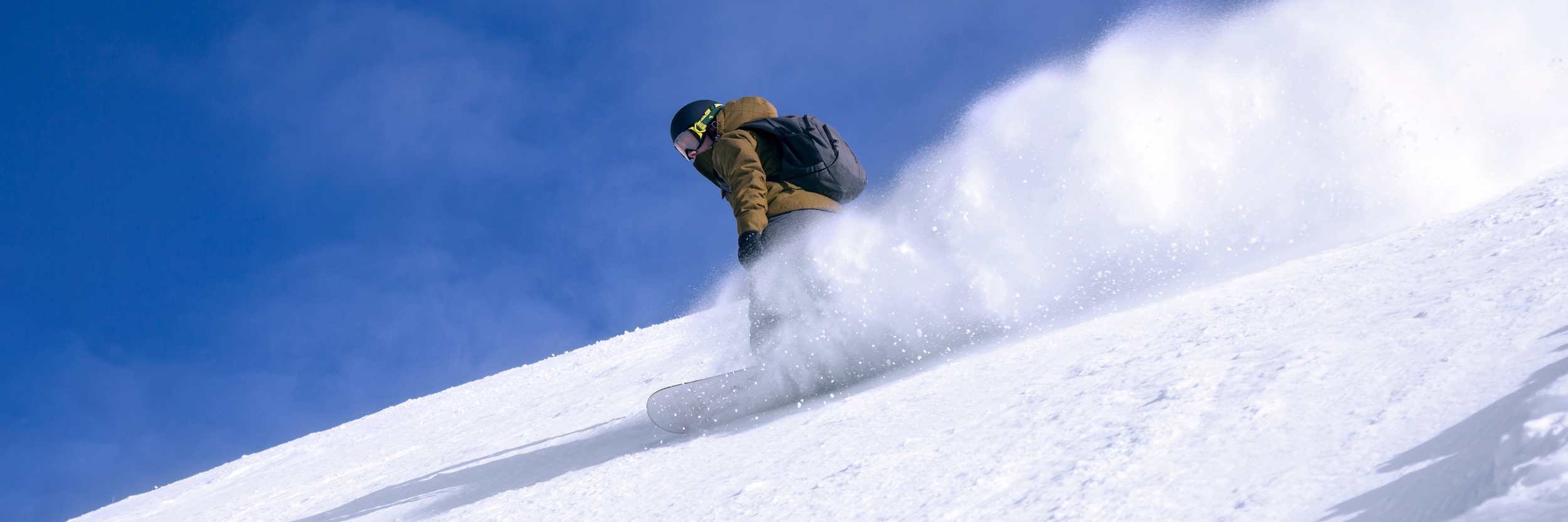 Person in winter gear skiing down a snowy slope under a clear blue sky.