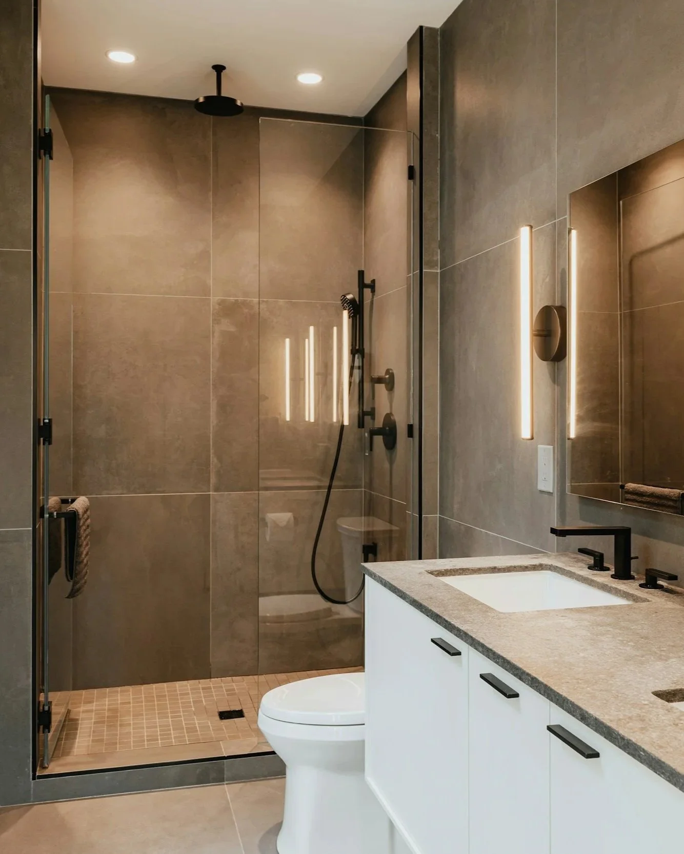 Modern bathroom with walk-in shower, black fixtures, and a vanity with a stone countertop and mirror.
