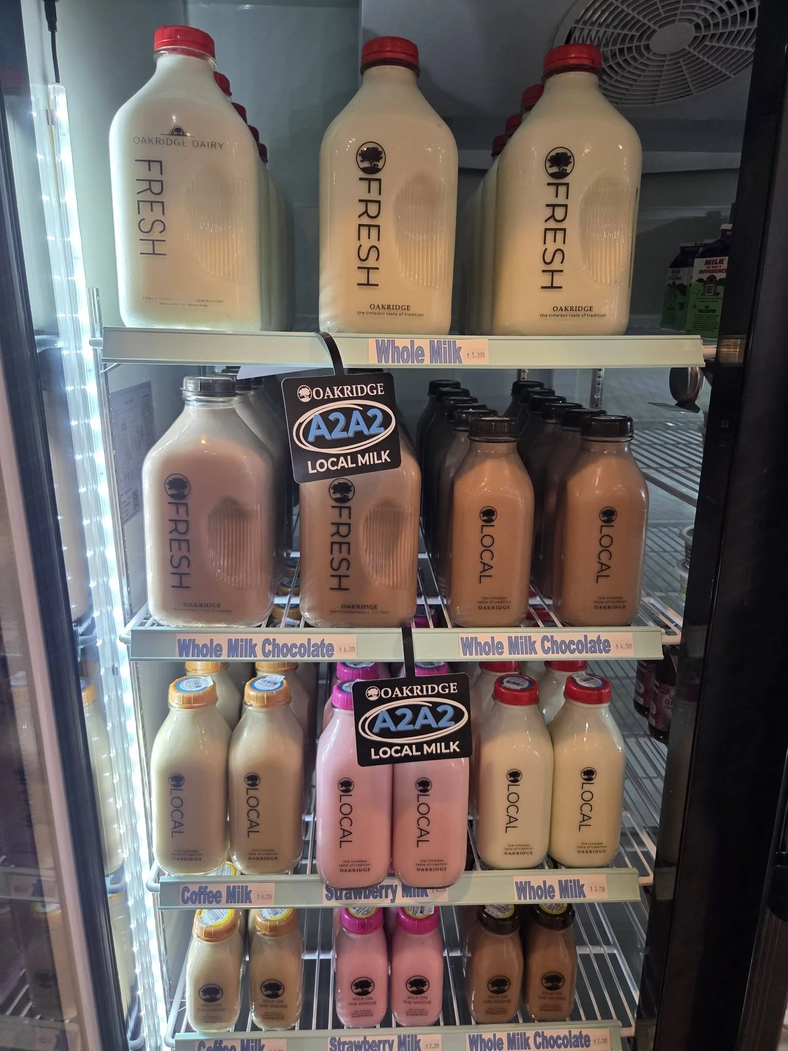 Refrigerator door with bottles of milk labeled 'Fresh', 'Local Milk', 'Whole Milk', 'Strawberry Milk', and 'Coffee Milk' on shelves