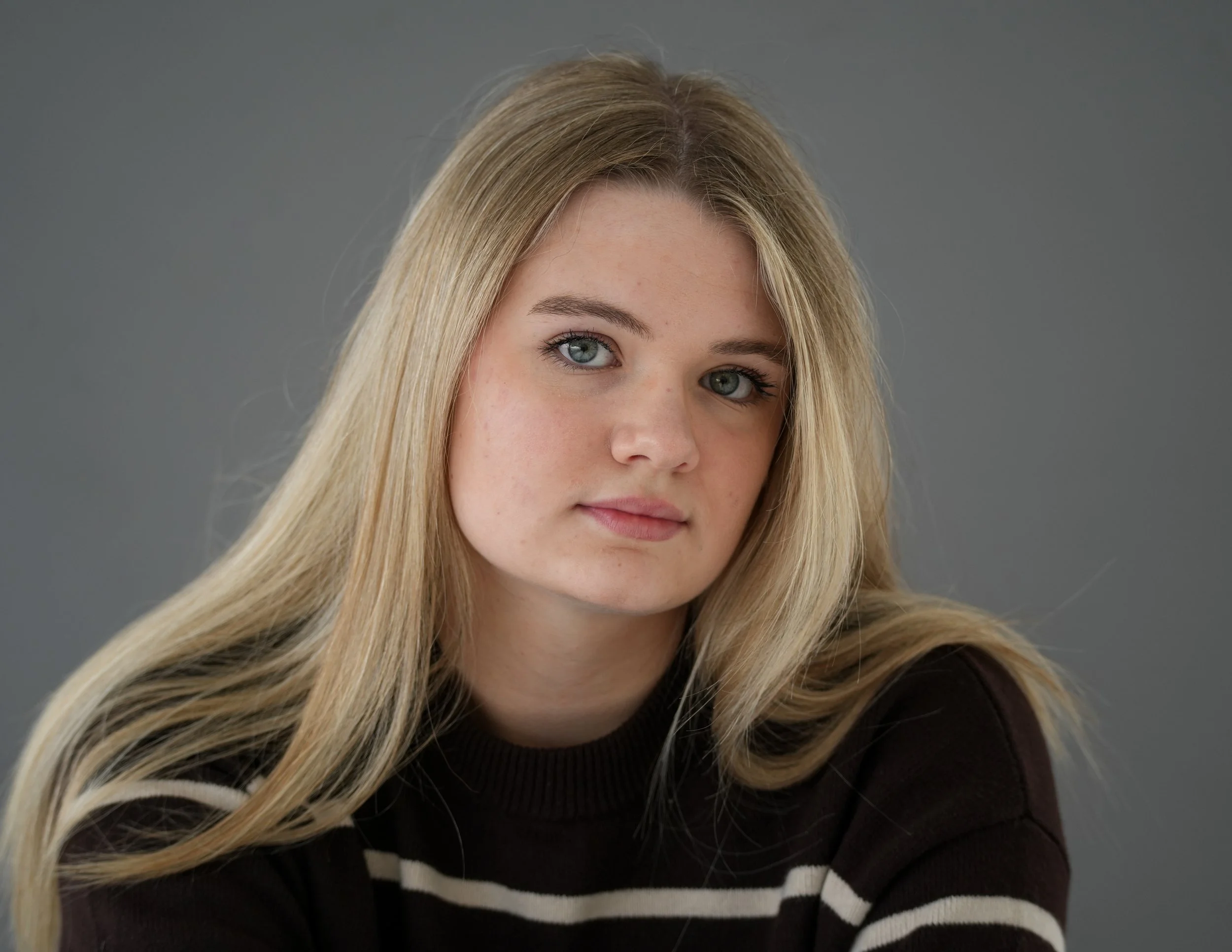 Young woman with long blonde hair and blue eyes, wearing a black and white striped top, looking at the camera.
