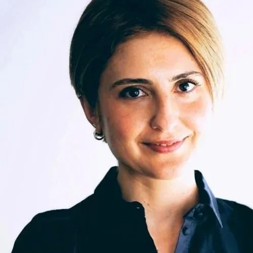 A woman with short, styled hair wearing a dark collared shirt, smiling at the camera.