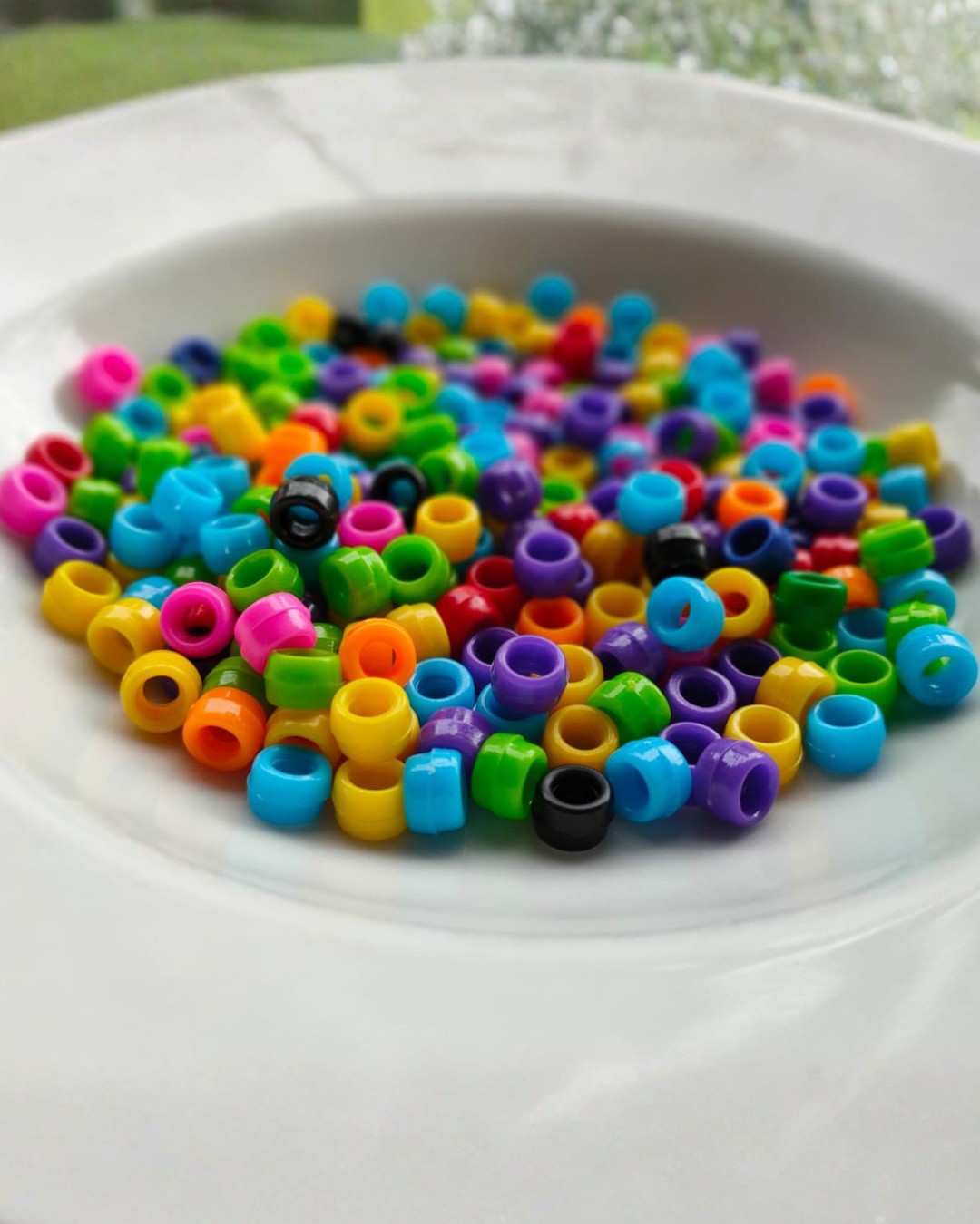 Varios pequeños abalorios de colores en un plato blanco.