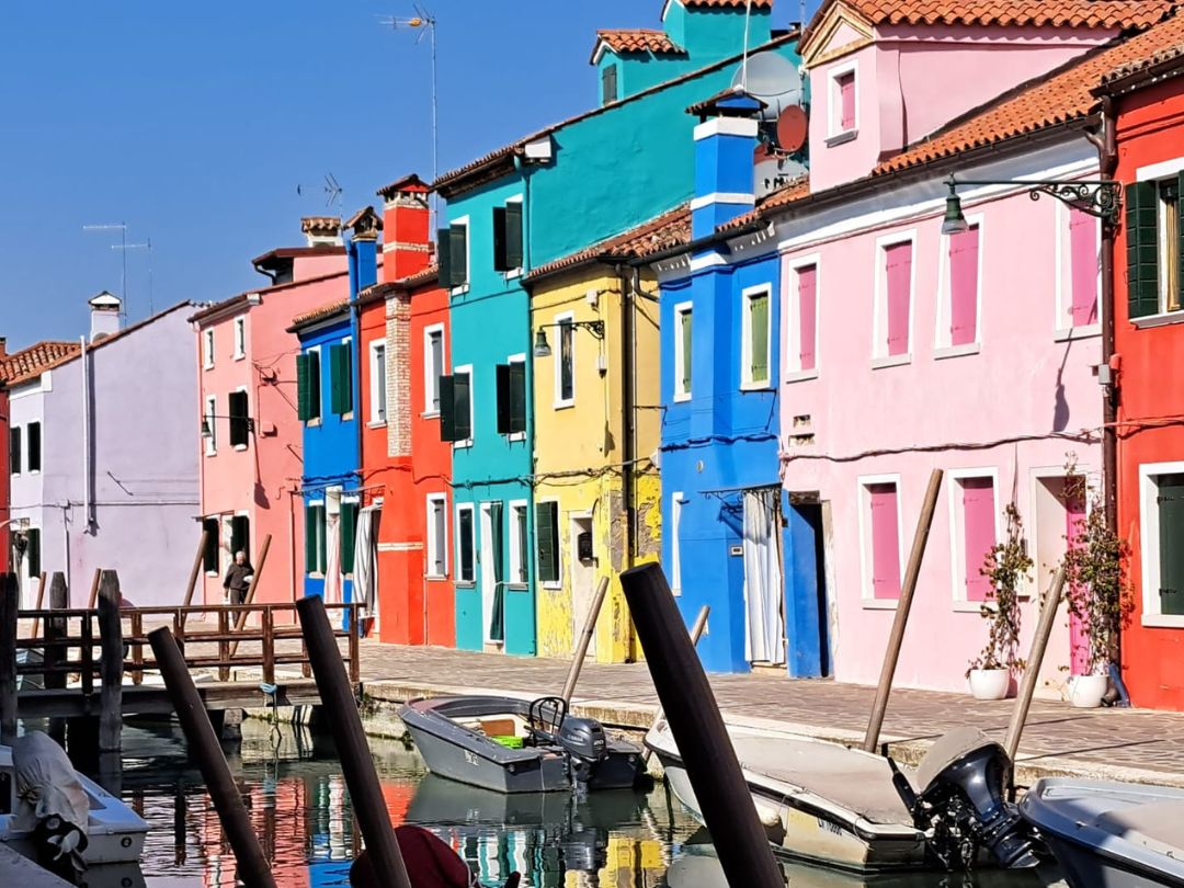 Casas coloridas a la orilla del agua con botes amarrados en un muelle, en un día soleado y despejado.