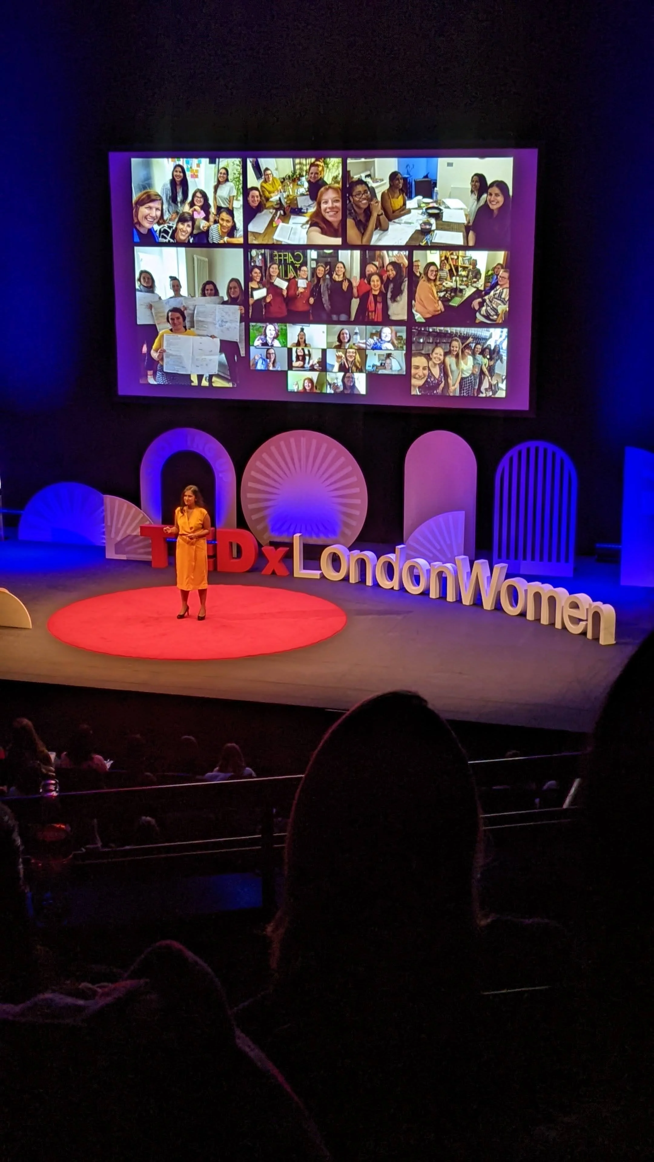 A woman giving a presentation on stage at a TEDx event about Money Movers. A large screen behind her displaying a collage of Money Mover participants in various group photos who engaged with taking climate action through personal finance.