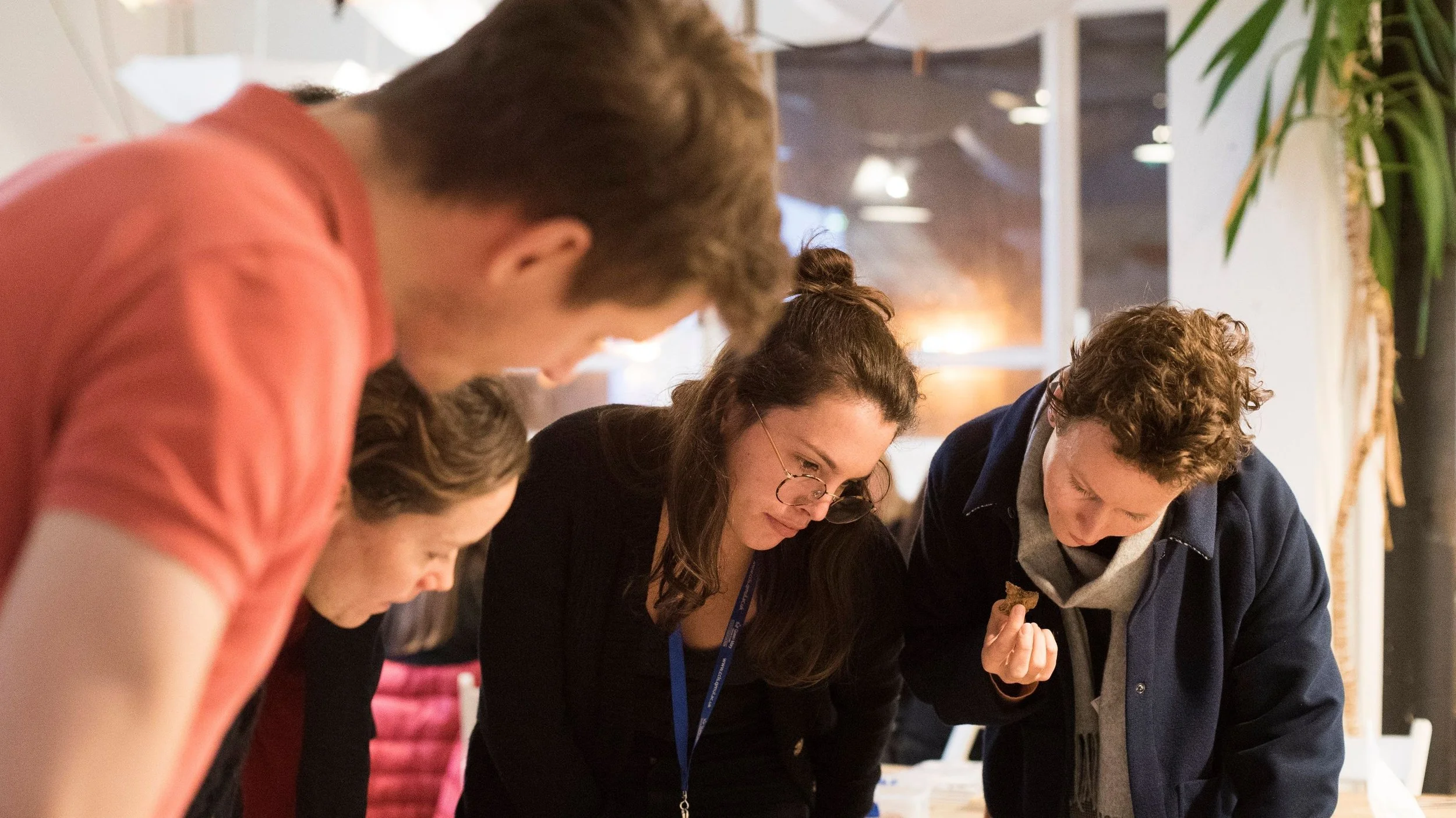 Four people closely examining something on a table in a well-lit indoor space.