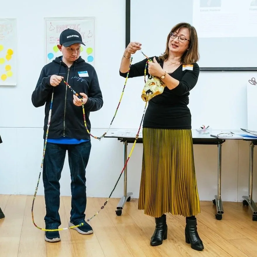 A woman and a boy holding a long beaded necklace together in the Economic Justice Huddles Showcase. Presenting on behalf of the SEND (Special Educational Needs and Disabilities) Seen Huddle. 