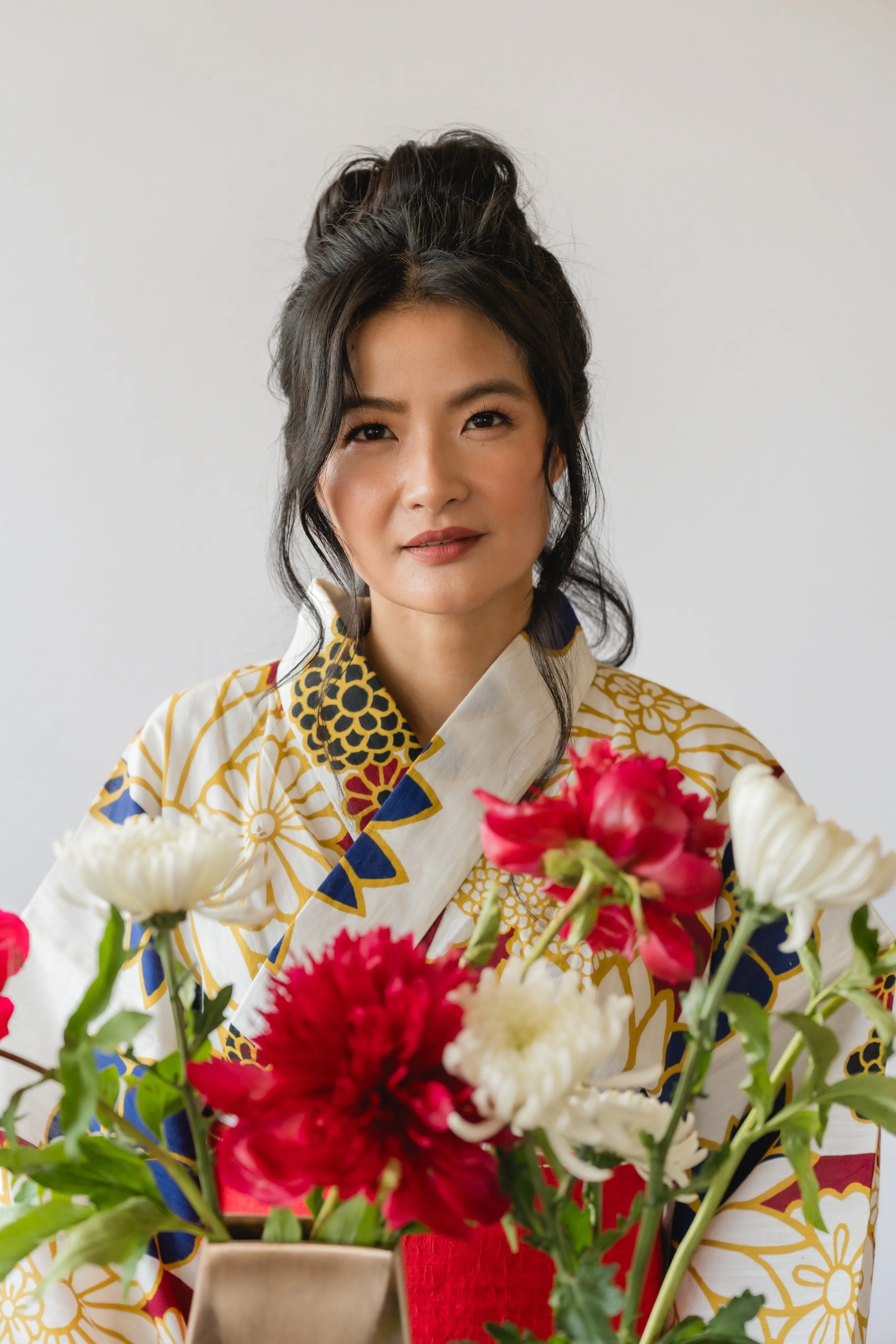 Woman dressed in a colorful kimono holding a bouquet of pink and white flowers.