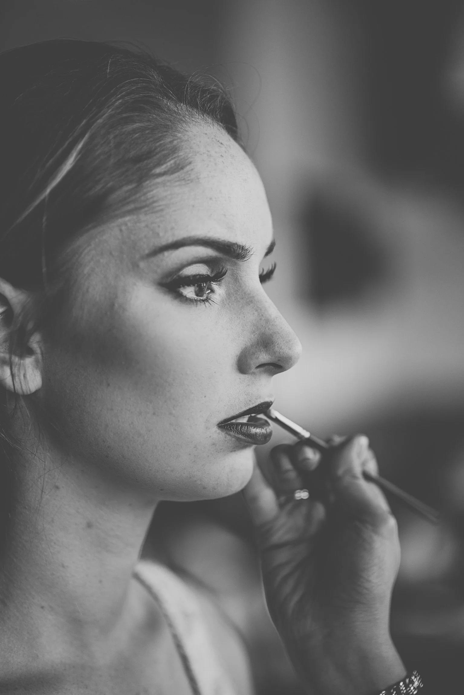 A woman with dark hair having makeup applied to her lips by a makeup artist