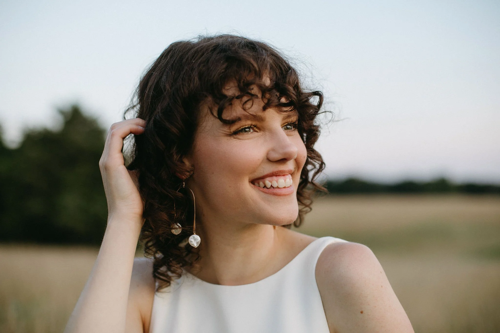 A woman with curly brown hair smiling outdoors during daytime.