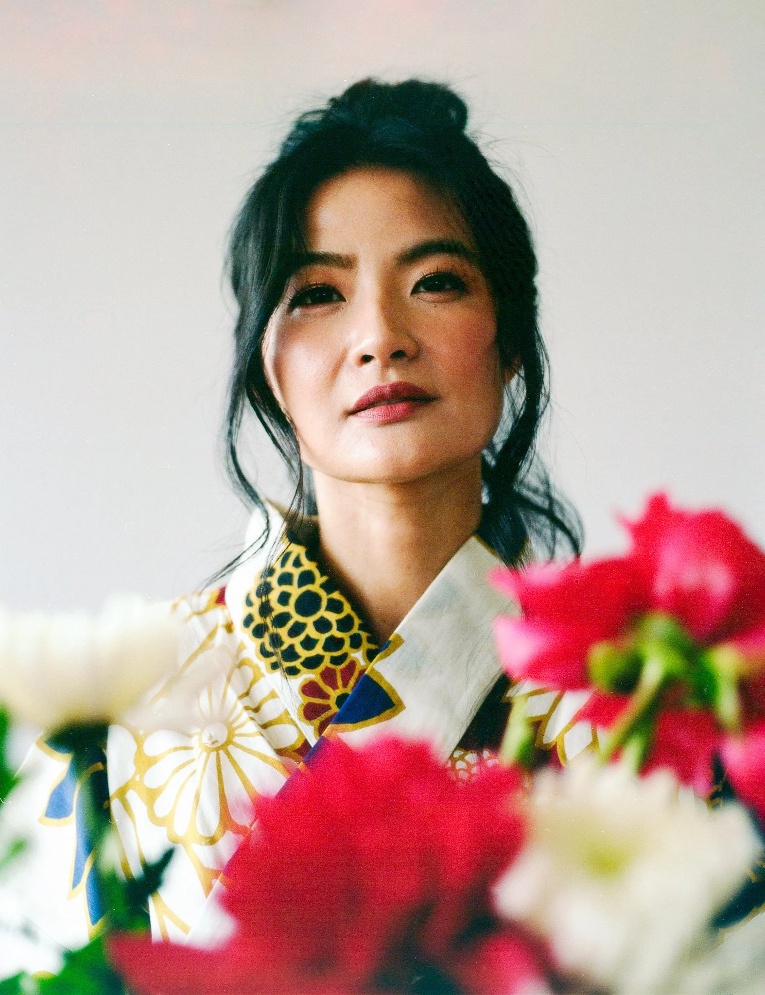 A woman wearing a traditional Japanese kimono, with a floral pattern, surrounded by pink and white flowers.