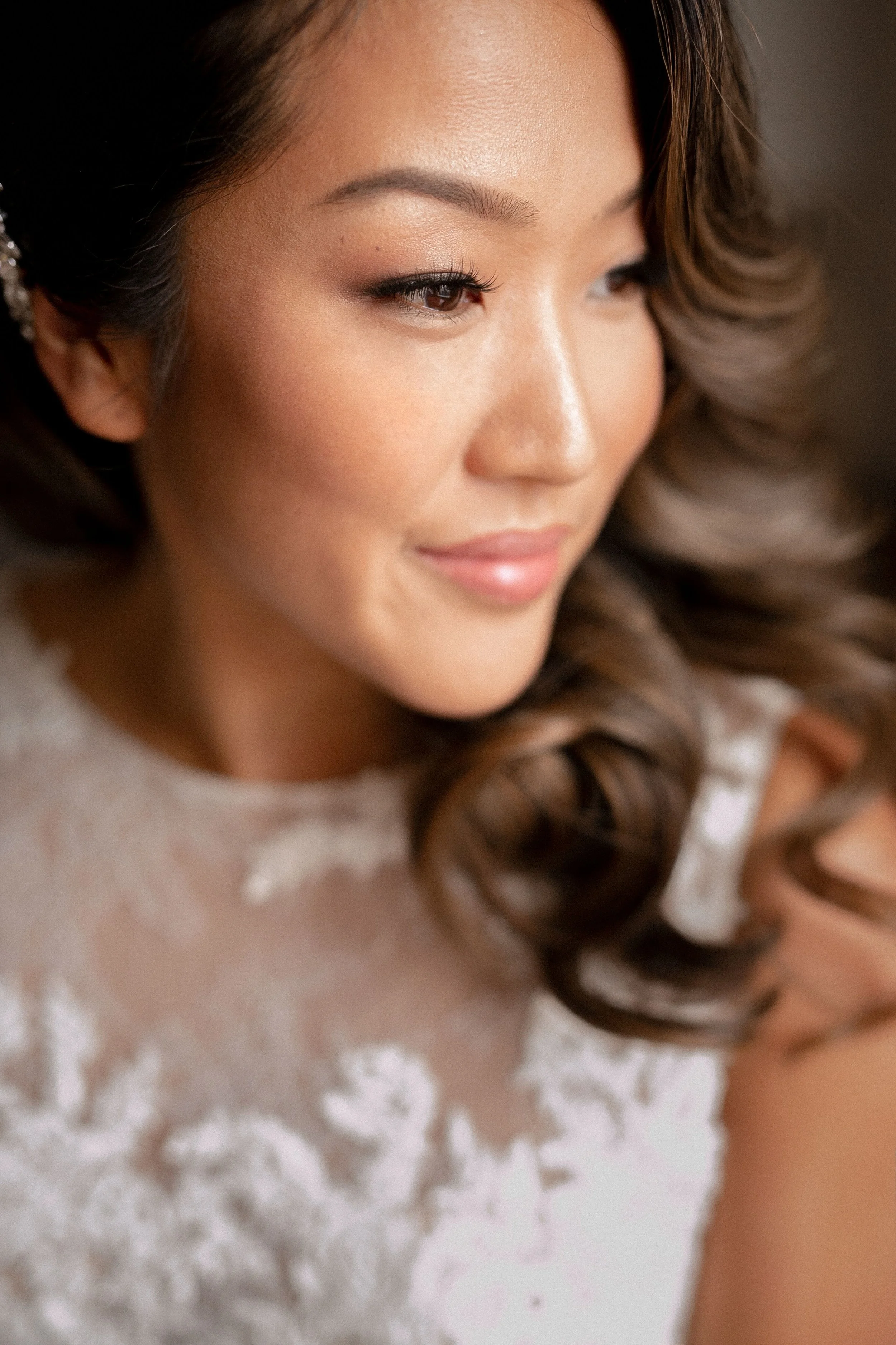 Close-up of a smiling woman with styled brown hair, makeup, and wearing a lace dress.