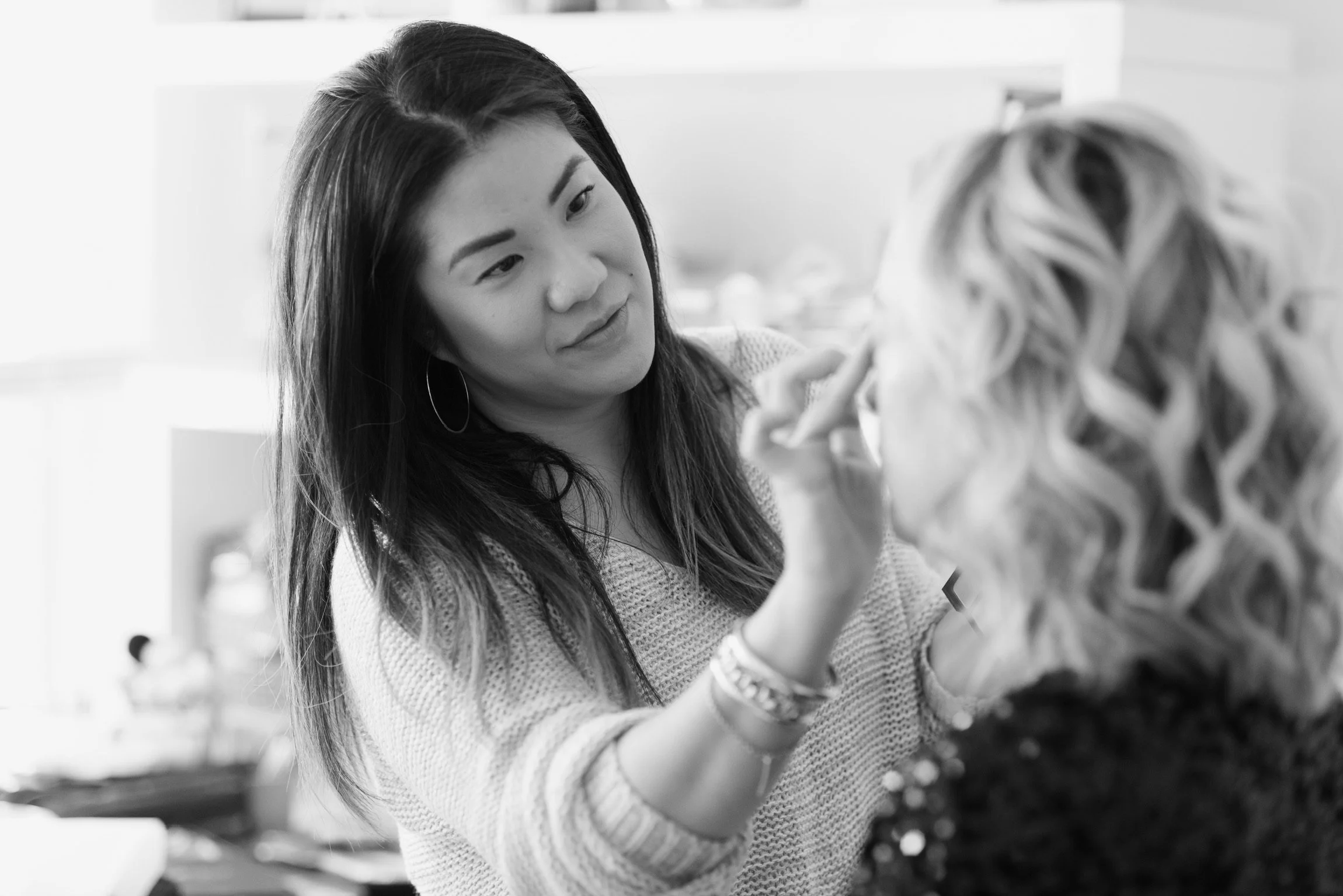 Makeup artist applying makeup to a woman's face in a salon setting.
