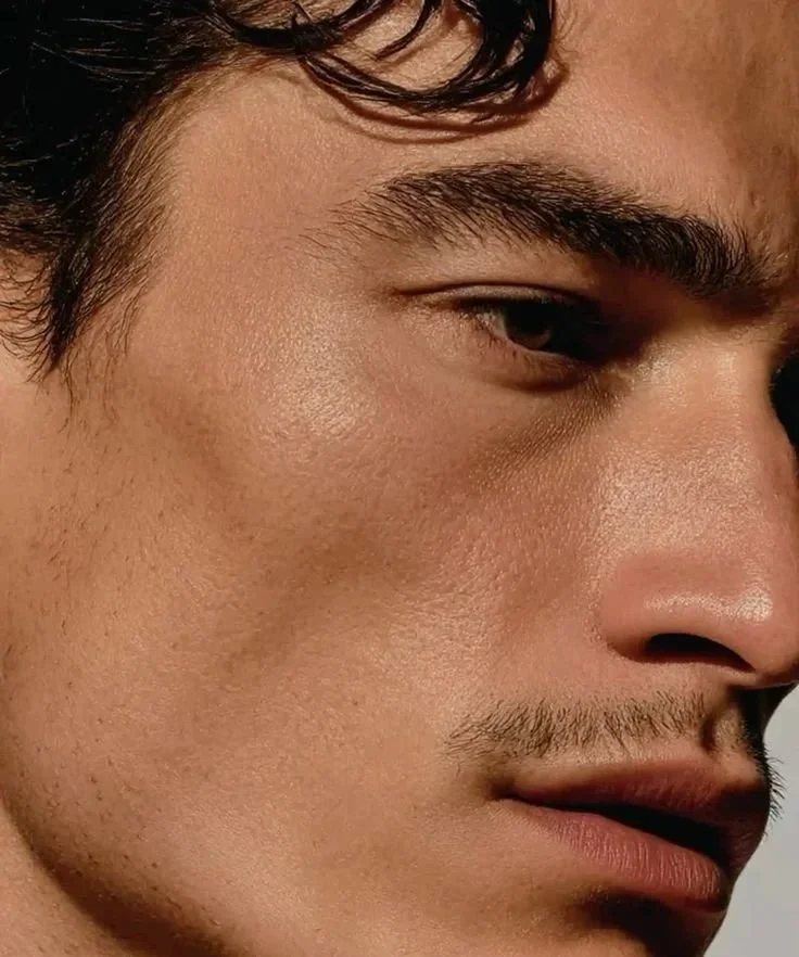 Près d'un visage masculin, gros plan sur le visage, avec des traits précis, peau claire, cheveux sombres, et regard légèrement downward.