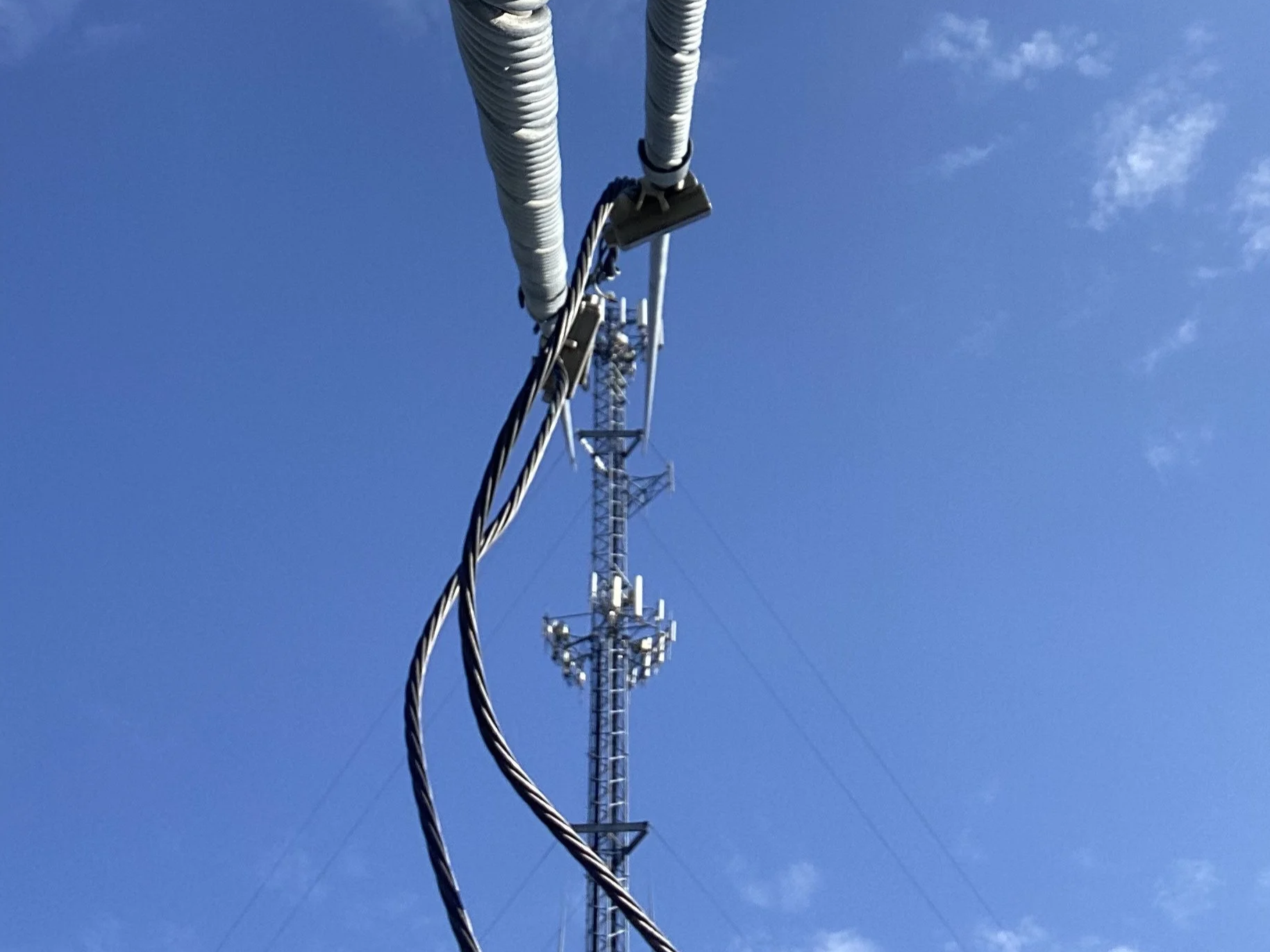 Close-up view of telecommunications tower and cables against blue sky with some clouds.