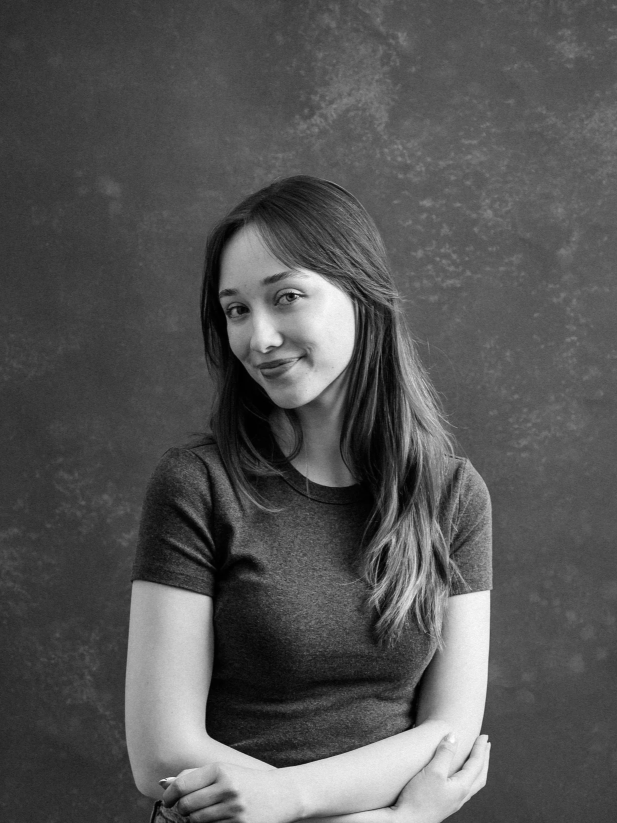 Me! A woman with long hair wearing a dark t-shirt, smiling with her arms crossed, sitting against a textured background.
