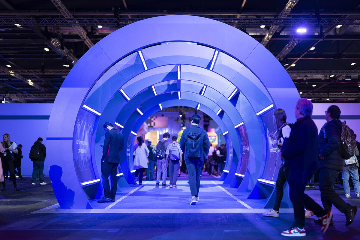 A futuristic, illuminated blue tunnel at a technology exhibition with people walking through it.