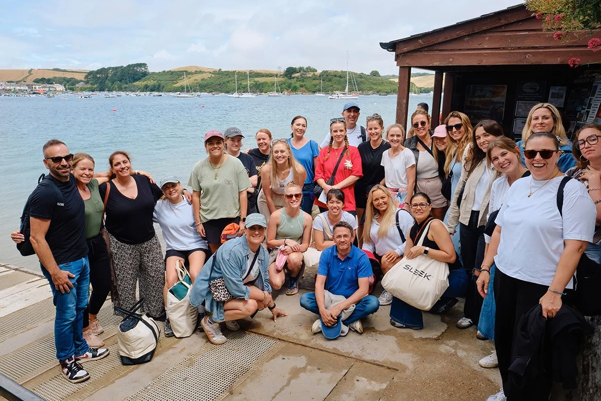 Group of people posing for a photo by a waterfront with boats and sailboats in the background