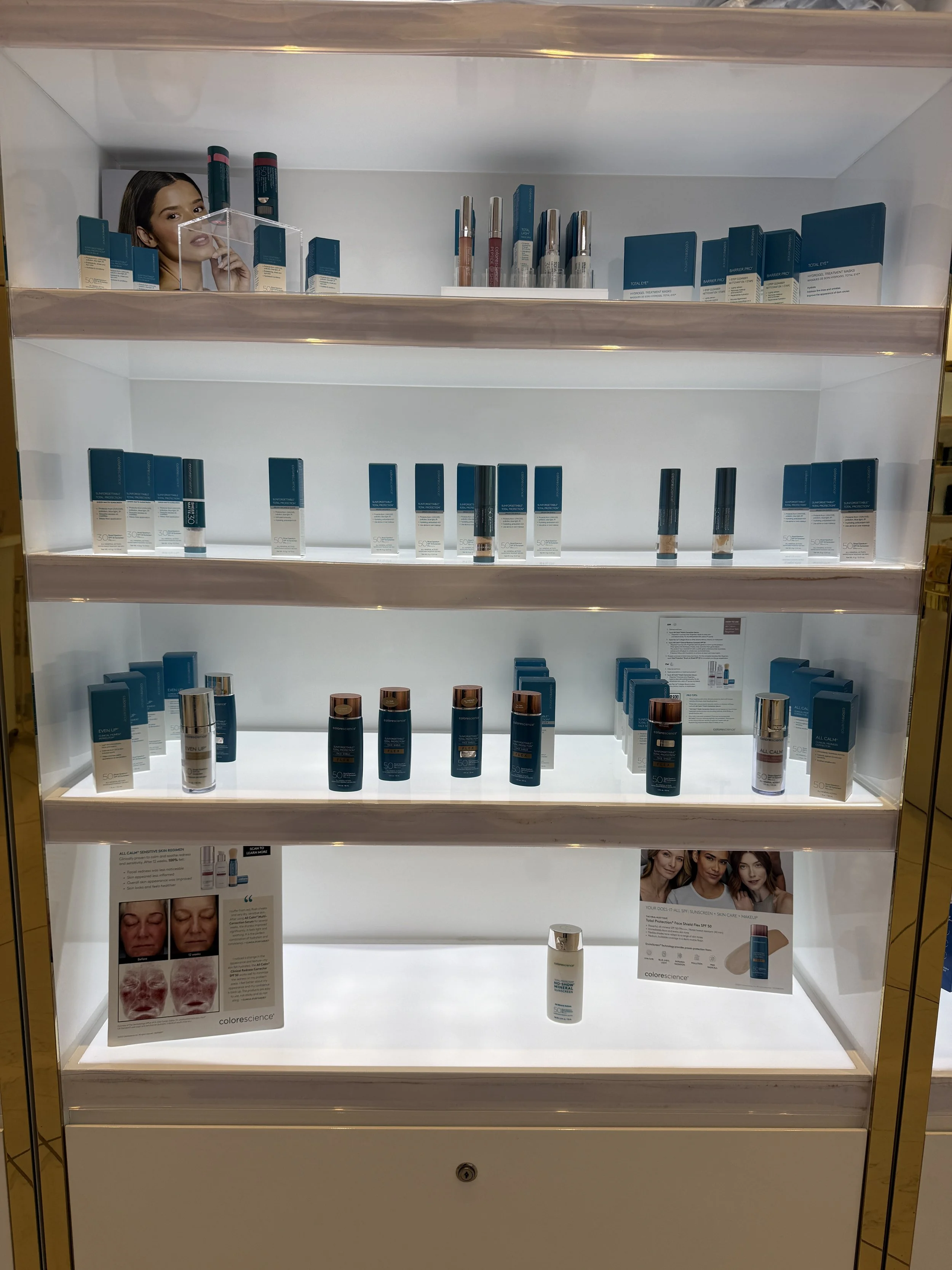 Display case with skincare products, mostly blue and white packaging, shelves illuminated, with promotional posters and skincare images.