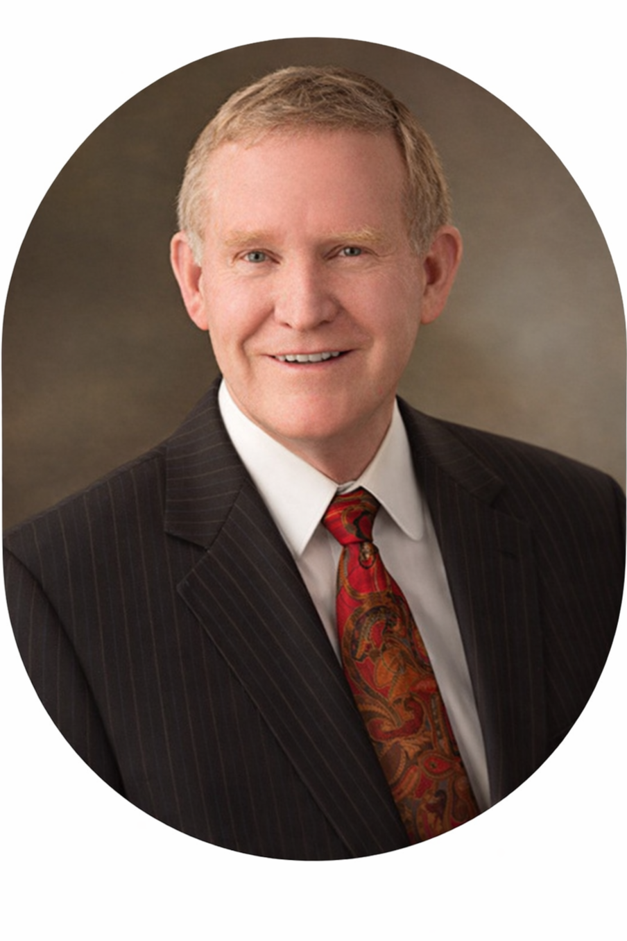 A middle-aged man with light hair wearing a dark pinstripe suit, white dress shirt, and a colorful paisley tie, smiling at the camera.