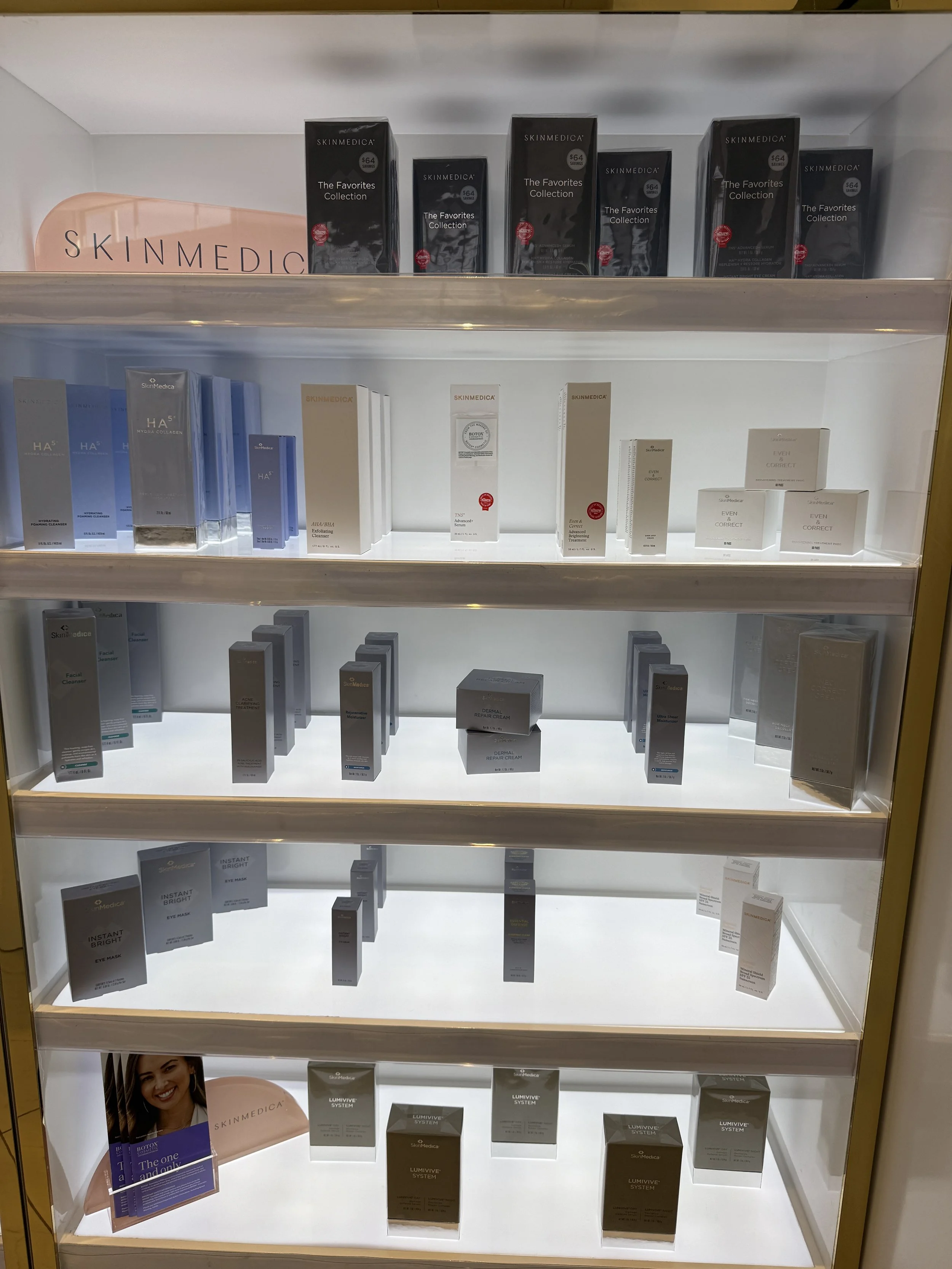 Display shelf with SKINMEDICA skincare products arranged on multiple illuminated shelves, including creams, serums, and masks in various packaging.
