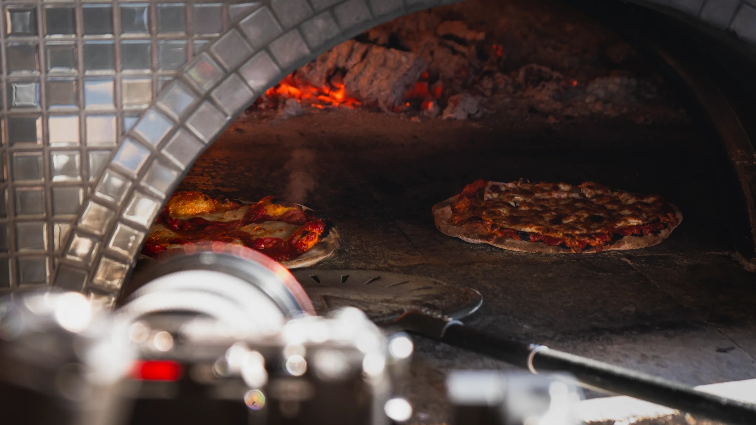 Deux pizzas en train de cuire dans un four à bois du vignoble, avec des flammes visibles en arrière-plan.