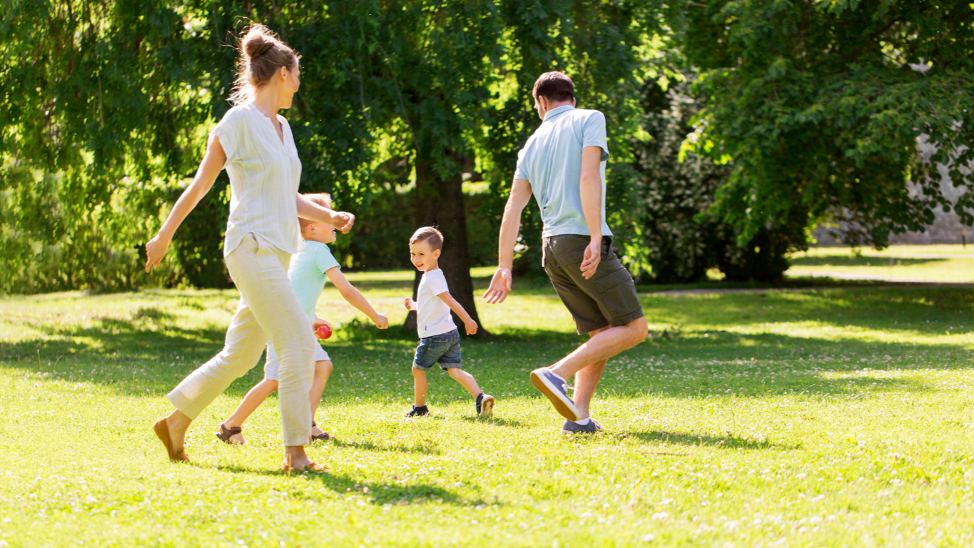 Family playing and running on a grassy park with trees in the background on a sunny day.