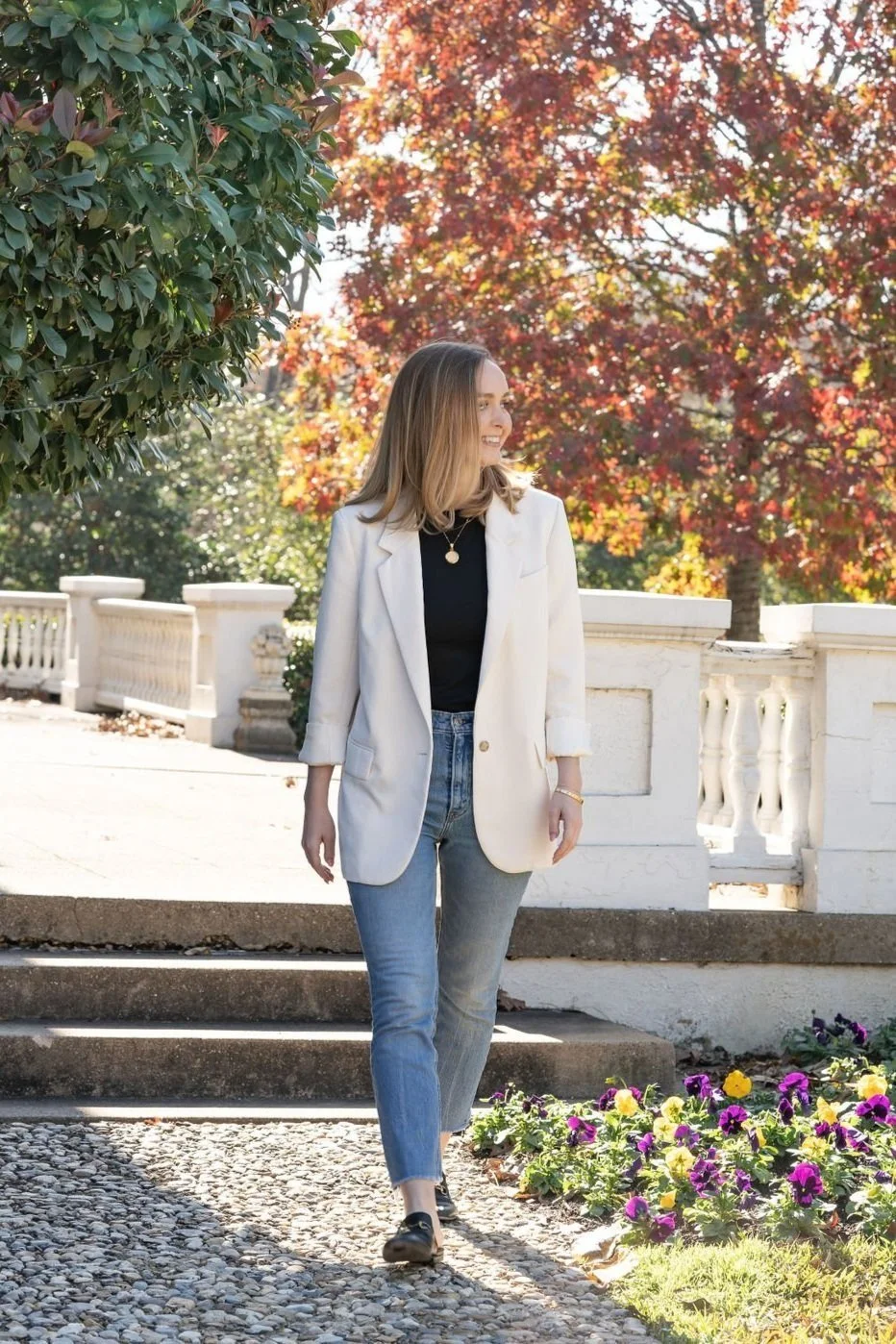 female landscape architect in blazer and jeans walking in a Dallas garden with autumn leaves and flowers.