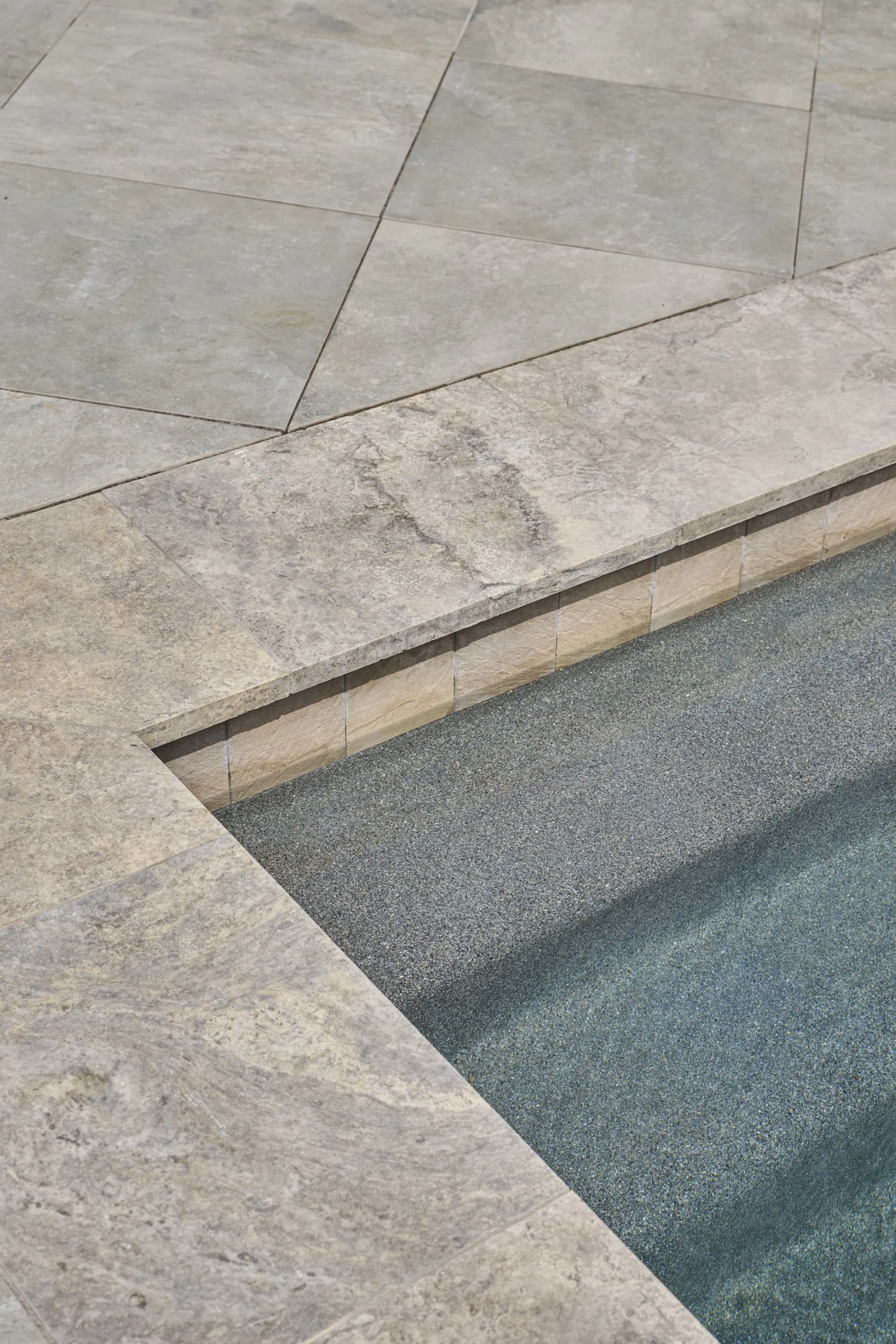 Backyard hardscape and landscape renovation complete with Porcelain Pavers, Belgard retaining walls, and evergreen planting design in North Dallas  | Designed by Caroline Higgins Design in Dallas, TX