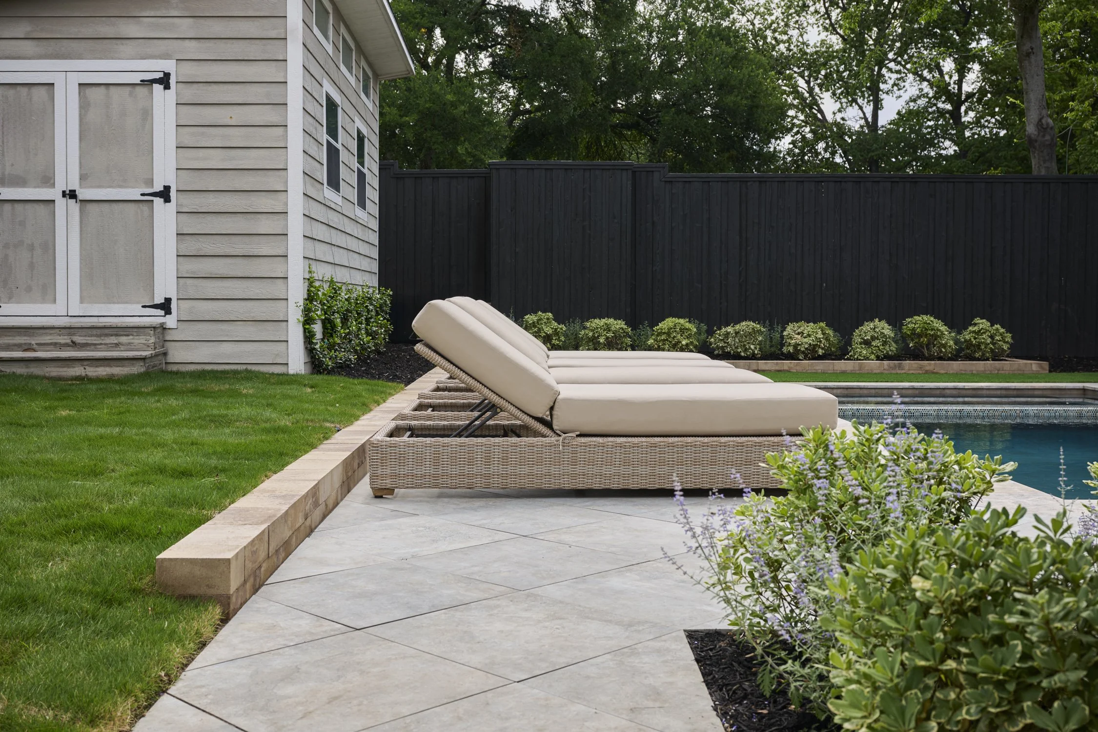 Backyard hardscape and landscape renovation complete with Porcelain Pavers, Belgard retaining walls, and evergreen planting design in North Dallas  | Designed by Caroline Higgins Design in Dallas, TX
