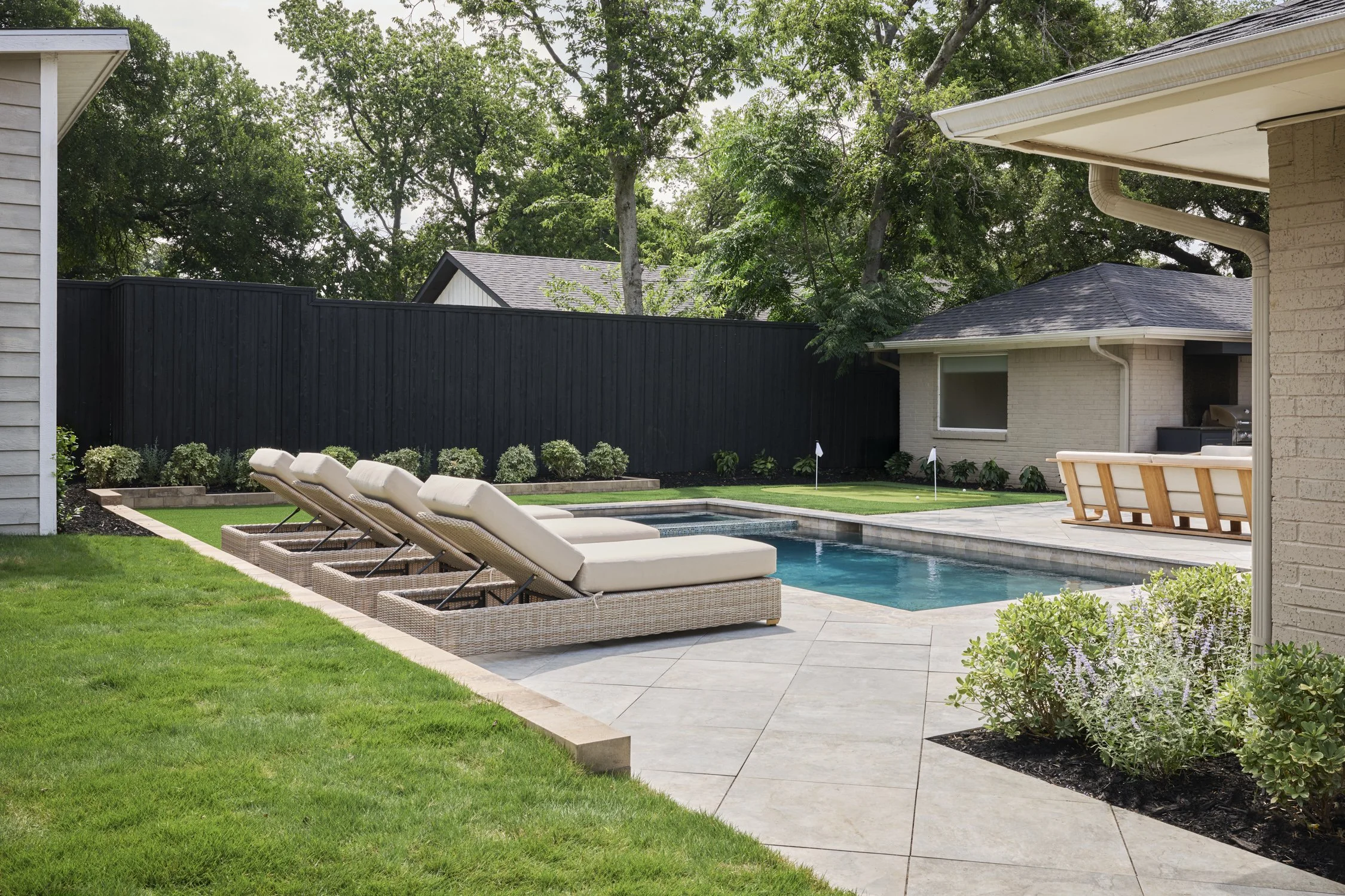 Backyard hardscape and landscape renovation complete with Porcelain Pavers, Belgard retaining walls, and evergreen planting design in North Dallas  | Designed by Caroline Higgins Design in Dallas, TX