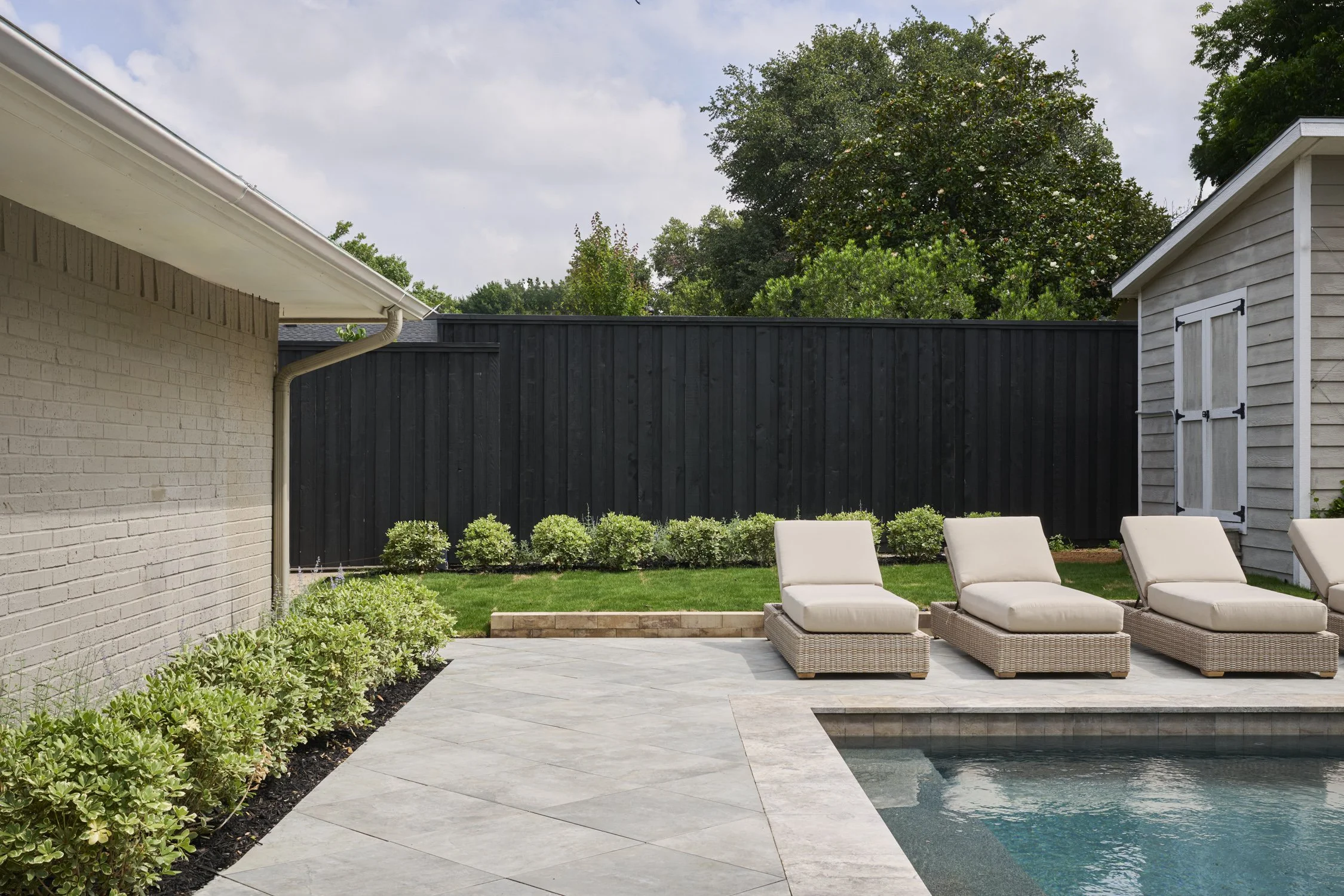 Backyard hardscape and landscape renovation complete with Porcelain Pavers, Belgard retaining walls, and evergreen planting design in North Dallas  | Designed by Caroline Higgins Design in Dallas, TX
