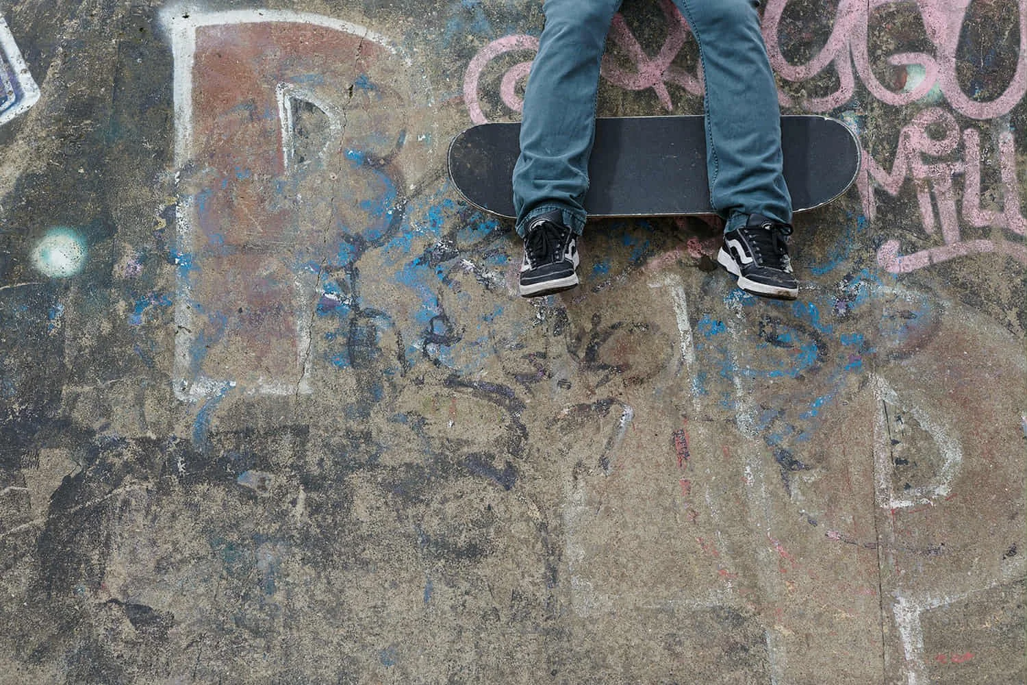 Person lying on a skateboard on a graffiti-covered pavement, seen from above.