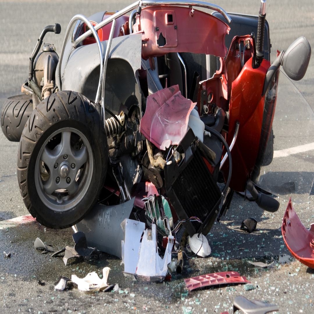 A wrecked red motorcycle with severe damage, lying on its side with broken parts and debris scattered around on the road.