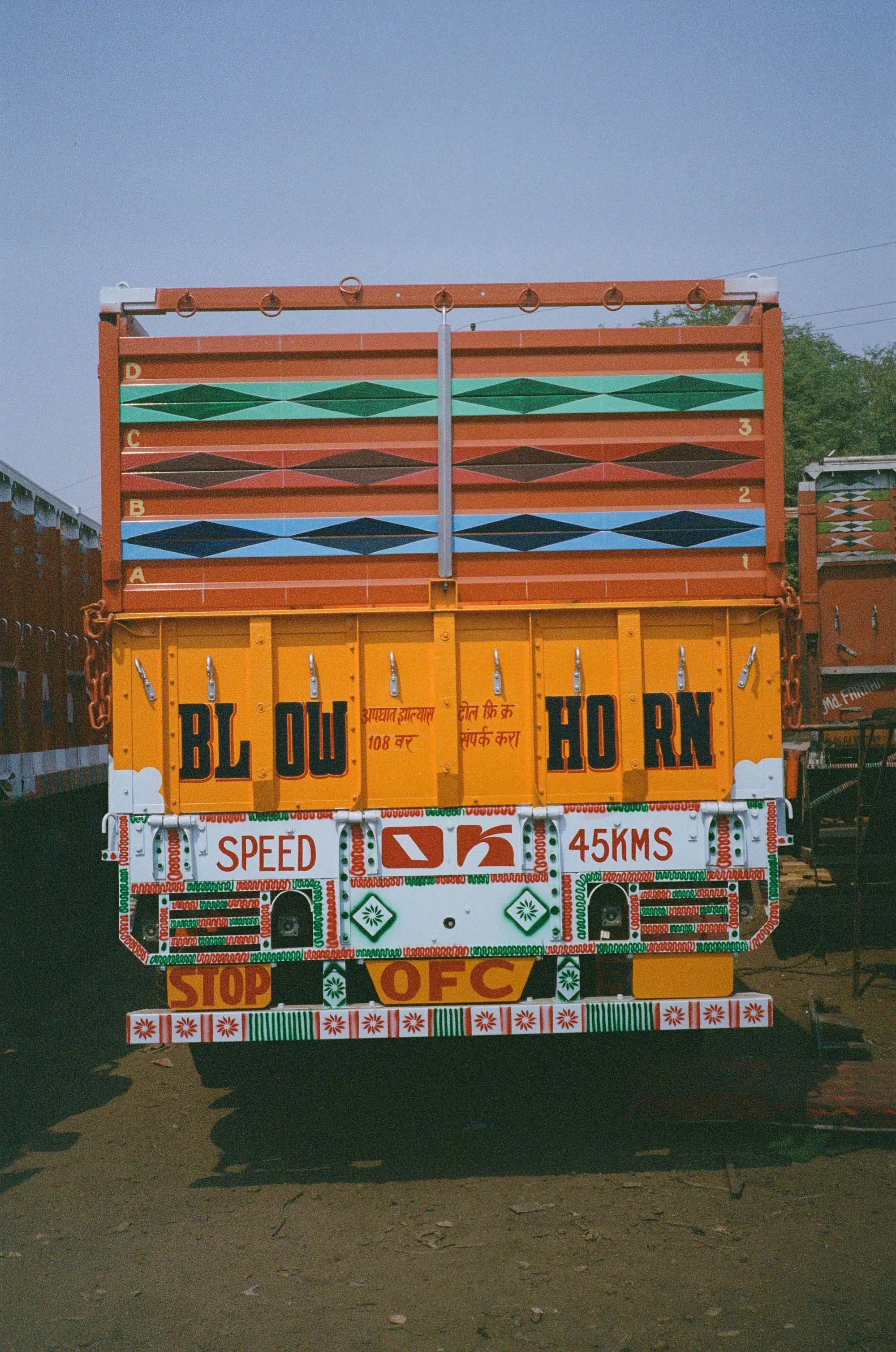 A colorful truck with intricate decorative patterns and writings, including 'BLOW HORN', 'SPEED 45 KMS', and 'STOP O.F.C.'