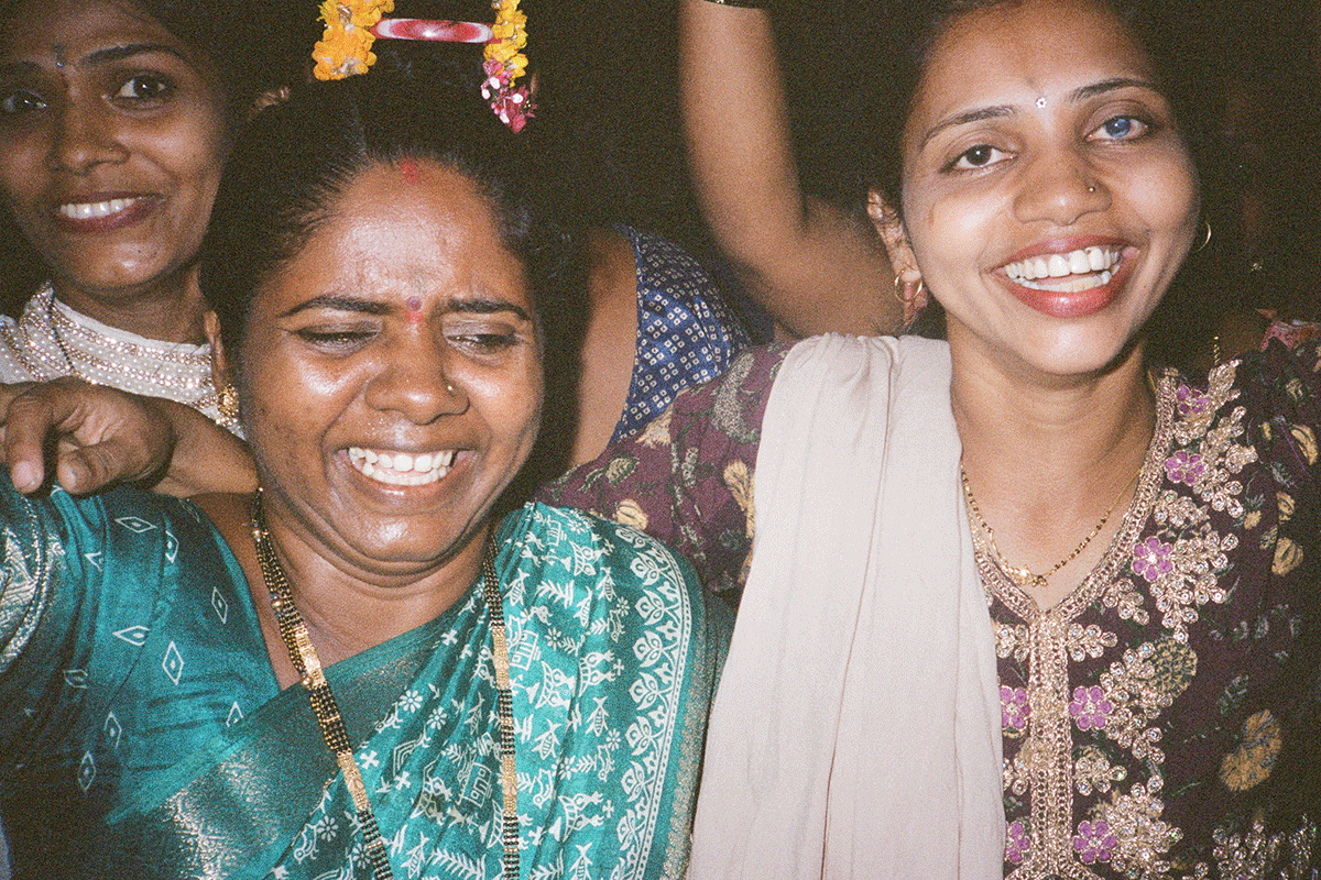 Three women smiling and celebrating at a festive event, dressed in traditional Indian attire and jewelry.